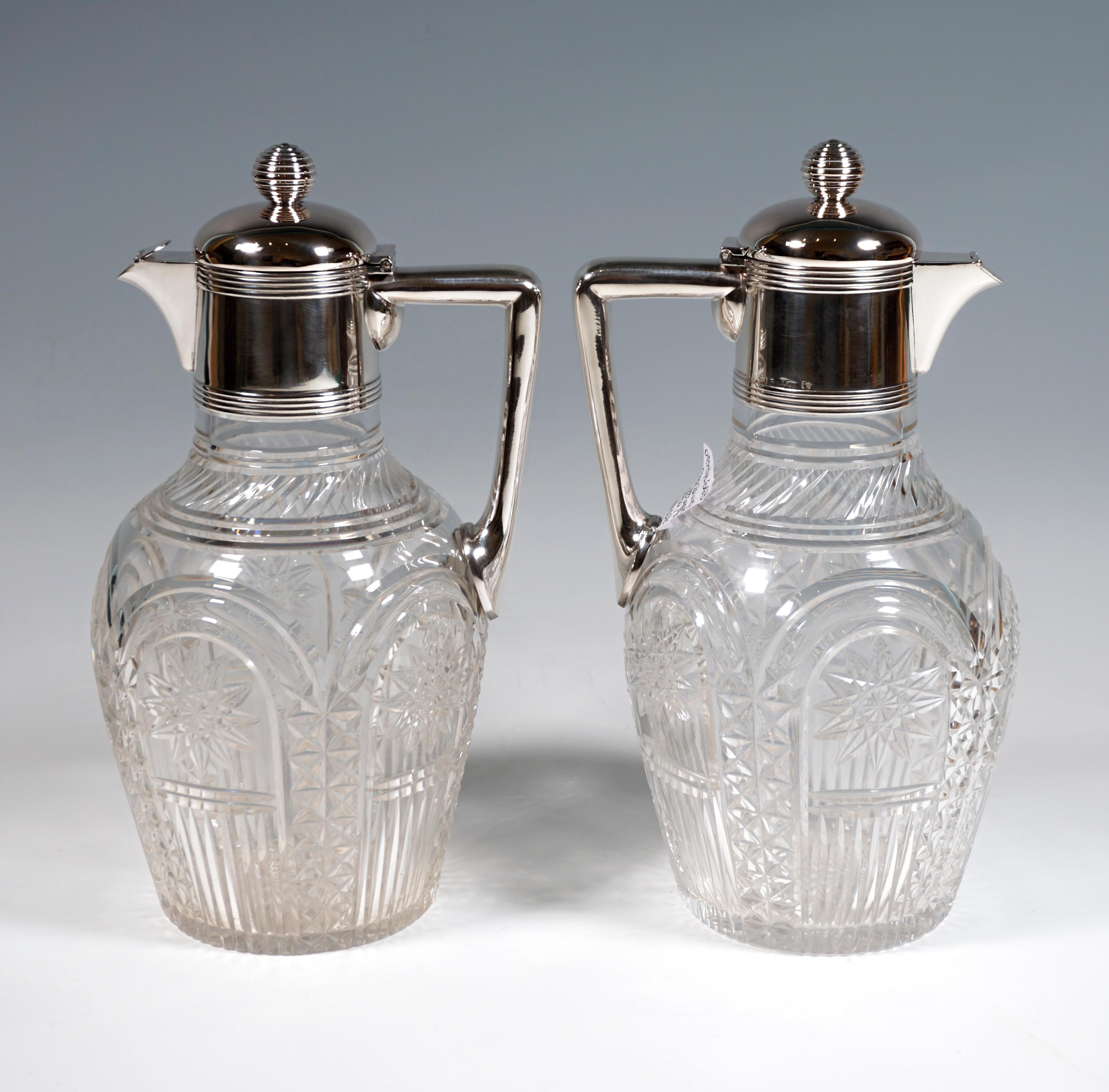 Two carafes made of clear glass with a raised, bulging body, surrounding five cut arches with stone cut decoration and cut suns in the arch segments, bevel cut at the base of the neck, bottom star, silver fittings grooved at the base and at the