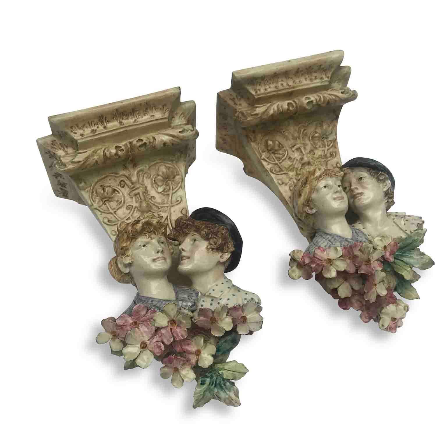 Pair of 20th century Art Nouveau Italian wall brackets, two hand-modeled, hand painted ceramic brackets with a fine polychrome decoration with half-bust girl and boy figures and flowers. 
They are a Northern Italy manufacture, unmarked, dating back