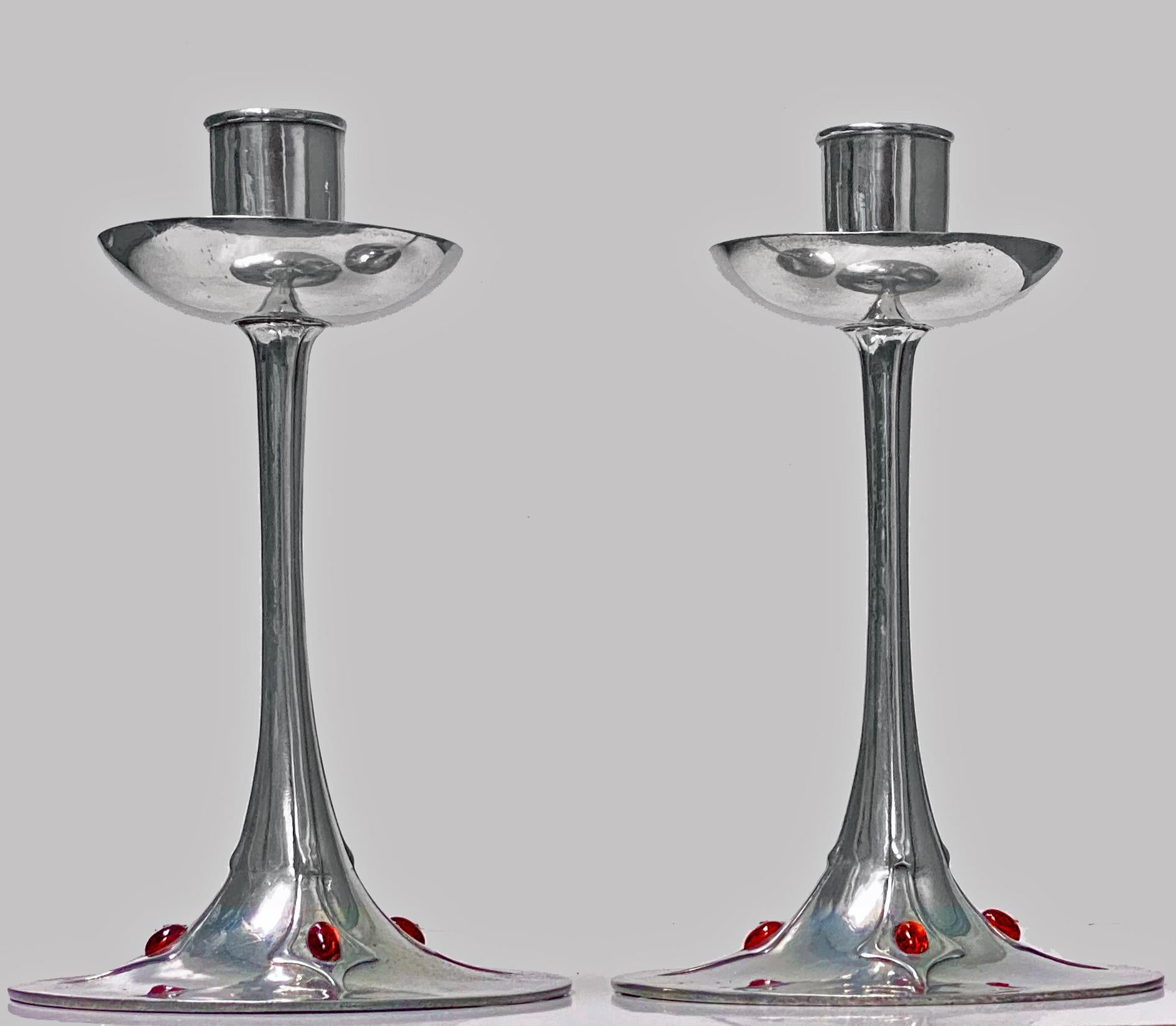 Pair of Art Nouveau Jugendstil Pewter candlesticks, circa 1910. Each on circular bases with stylized slightly tapered foliate stems set with four oval red glass cabochon stones rising to welled drip pans and plain sockets. Faint marks on bases and