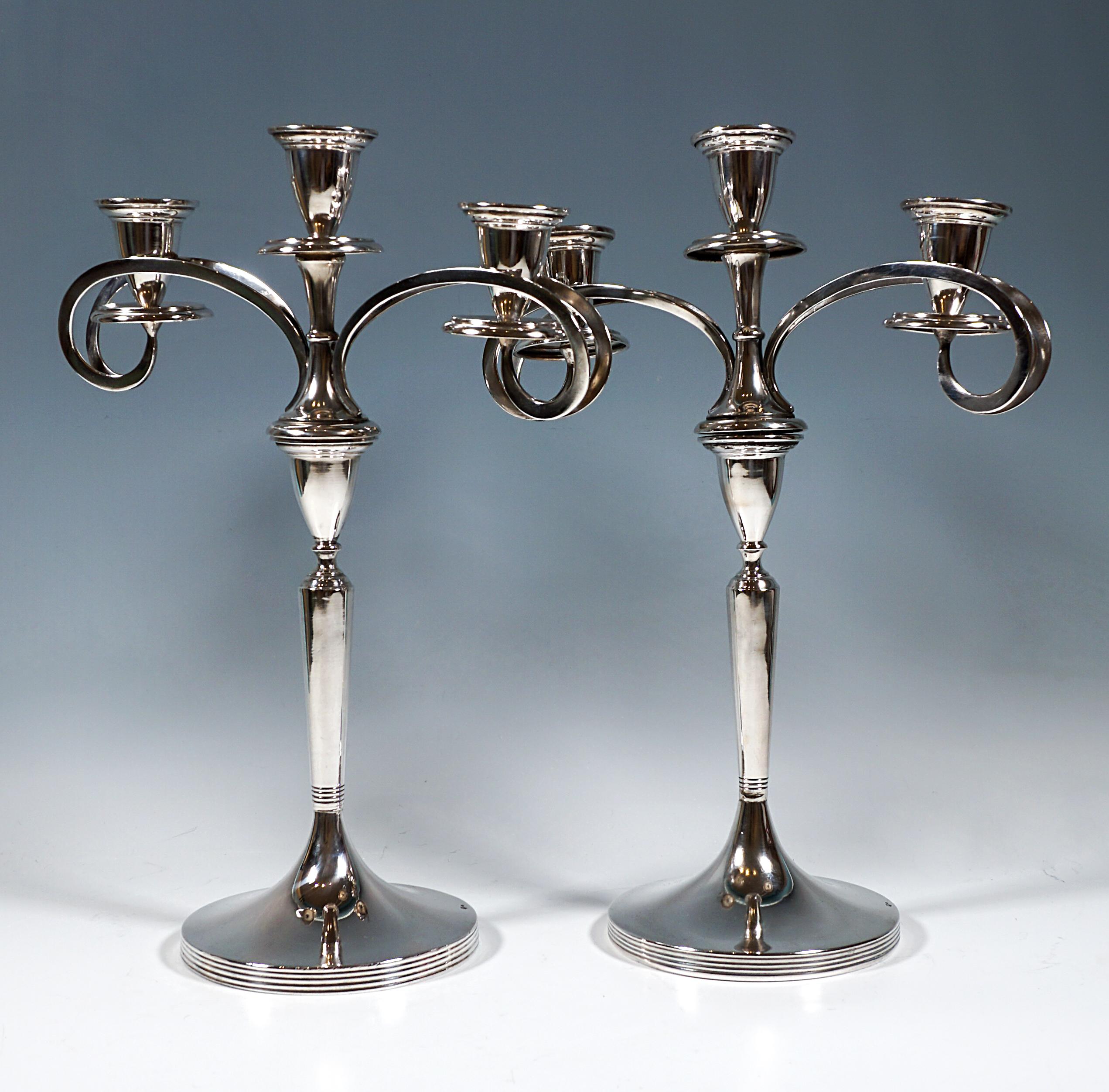 Dos elegantes y sencillos candelabros de plata sobre un soporte redondo, pie redondo acanalado en el lateral, fuste liso elevado en el centro con una constricción perfilada, fuste que se ensancha cónicamente hacia la parte superior, con una boquilla