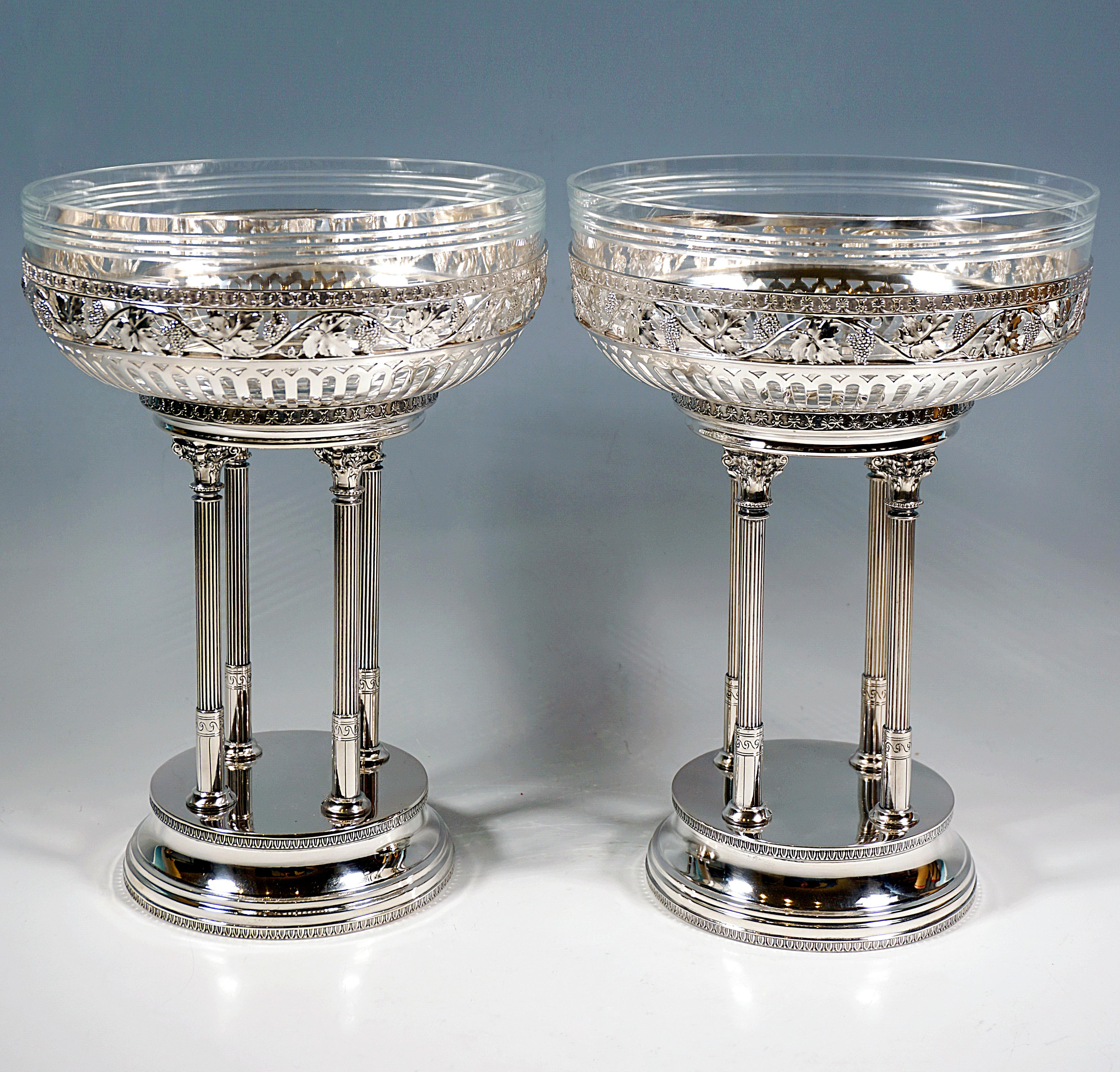 Two elegant silver centerpieces on a high, round, stepped base, bordered by palmette bands, arranged in a square, four slender, fluted columns with Corinthian-looking fantasy capitals, crowned by a projecting bowl, lamellar openwork in the lower