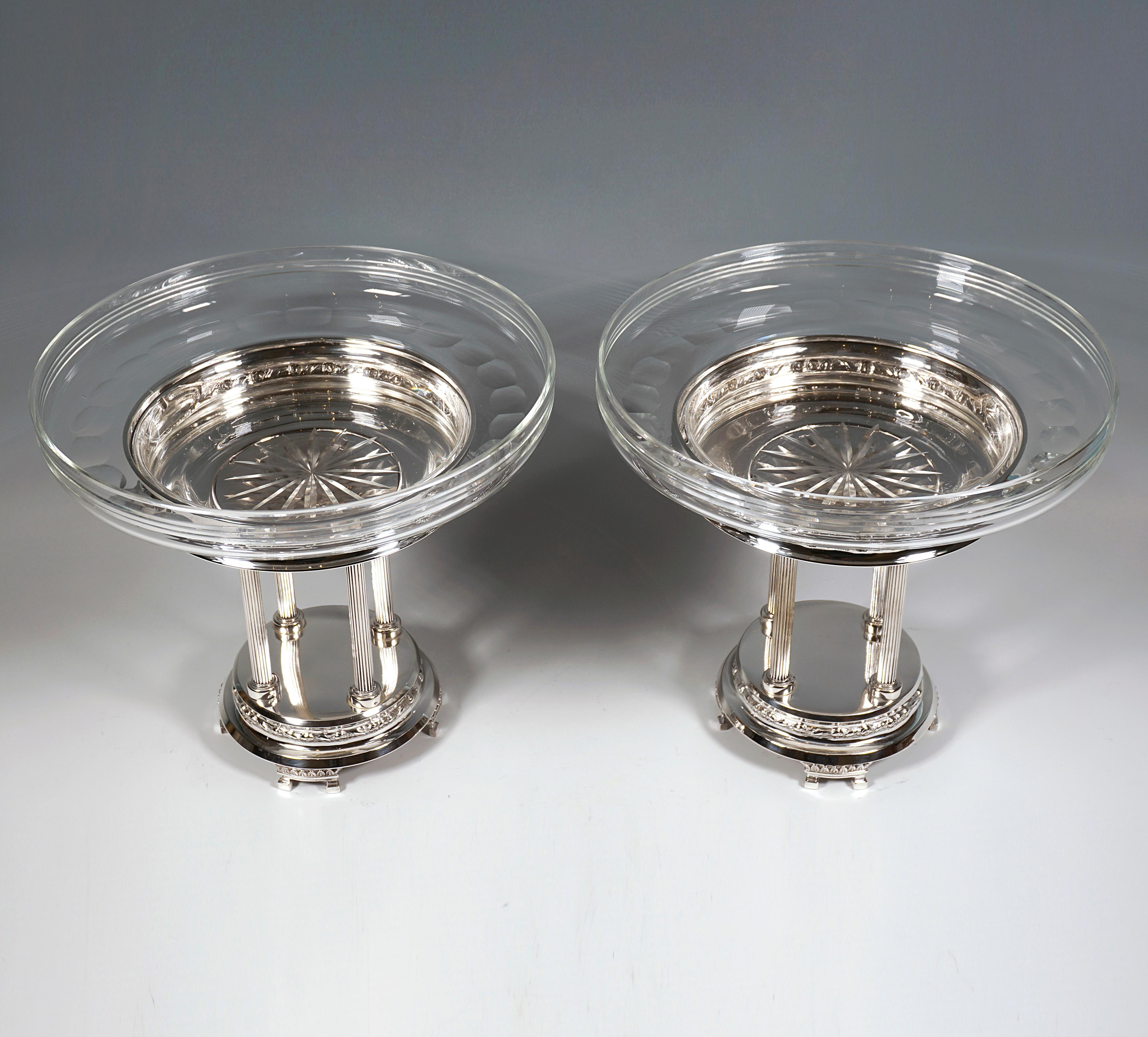 Two elegant silver centerpieces on a high, round, stepped base with a floral relief band, on four divided feet with palmette frieze, on top of which four slender fluted columns arranged in a square, crowned by a projecting silver 
bowl with a floral