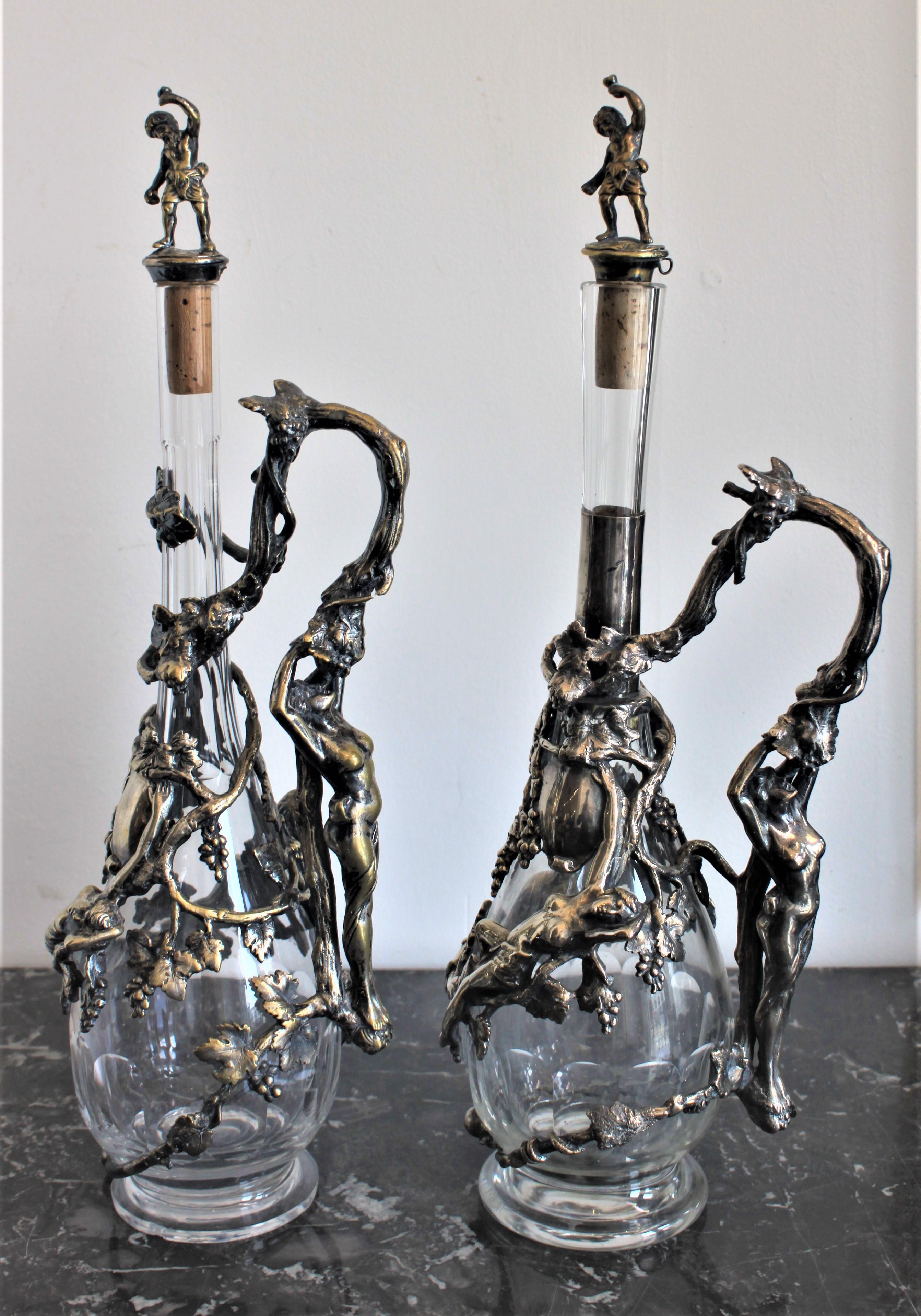 This pair of crystal decanters date from circa 1900 from the Art Nouveau period, and have their origins from Europe, and most likely Austria. The decanters are ornately decorated with figural grape vines done in silver plate with two figural nude