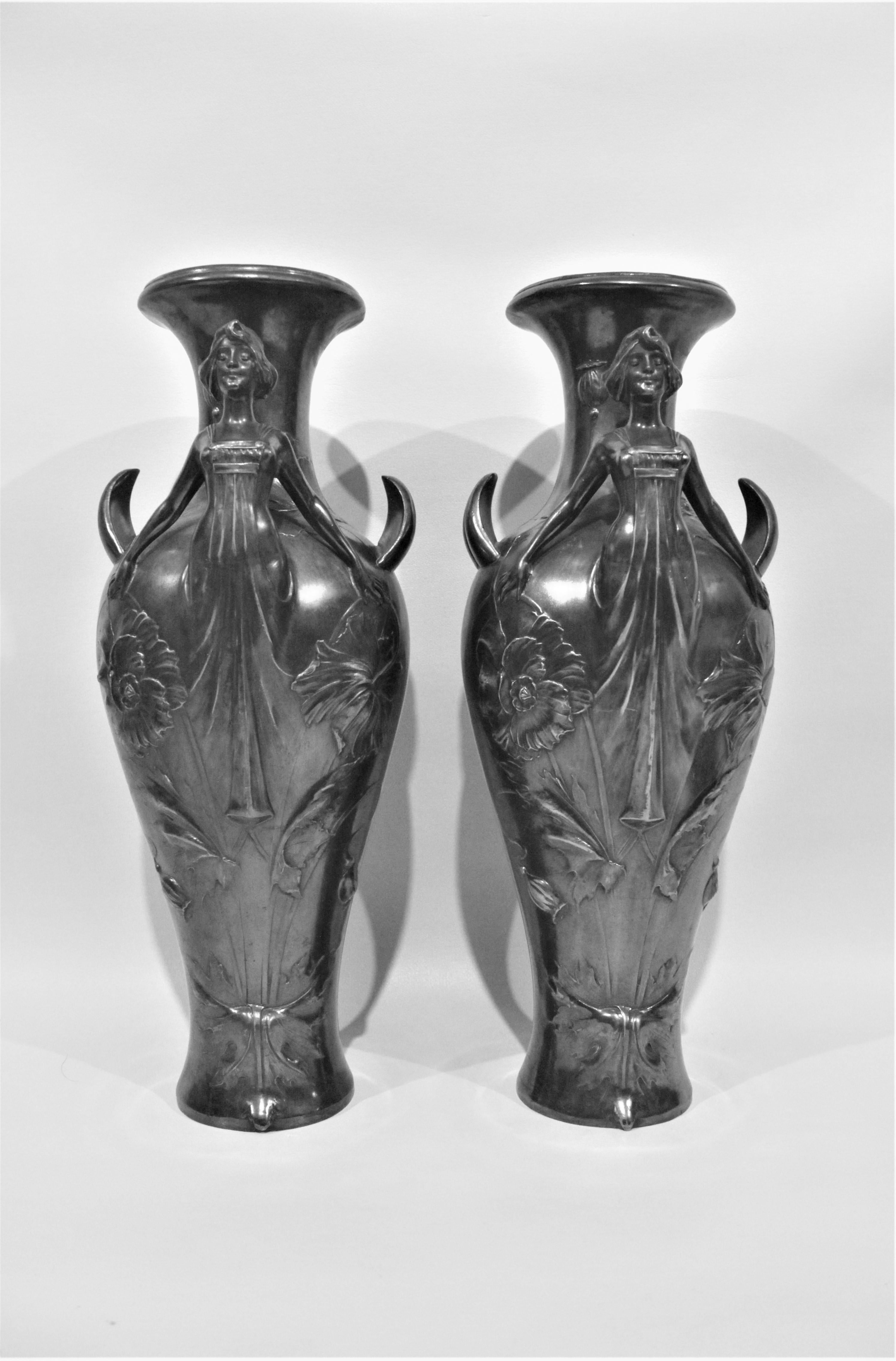 This matched pair of silver plated vases each depicting a stylized robed female with outstretched arms were mostly likely made in France, although are unmarked. The arms function as handles for the vases and the bodies of the women are quite
