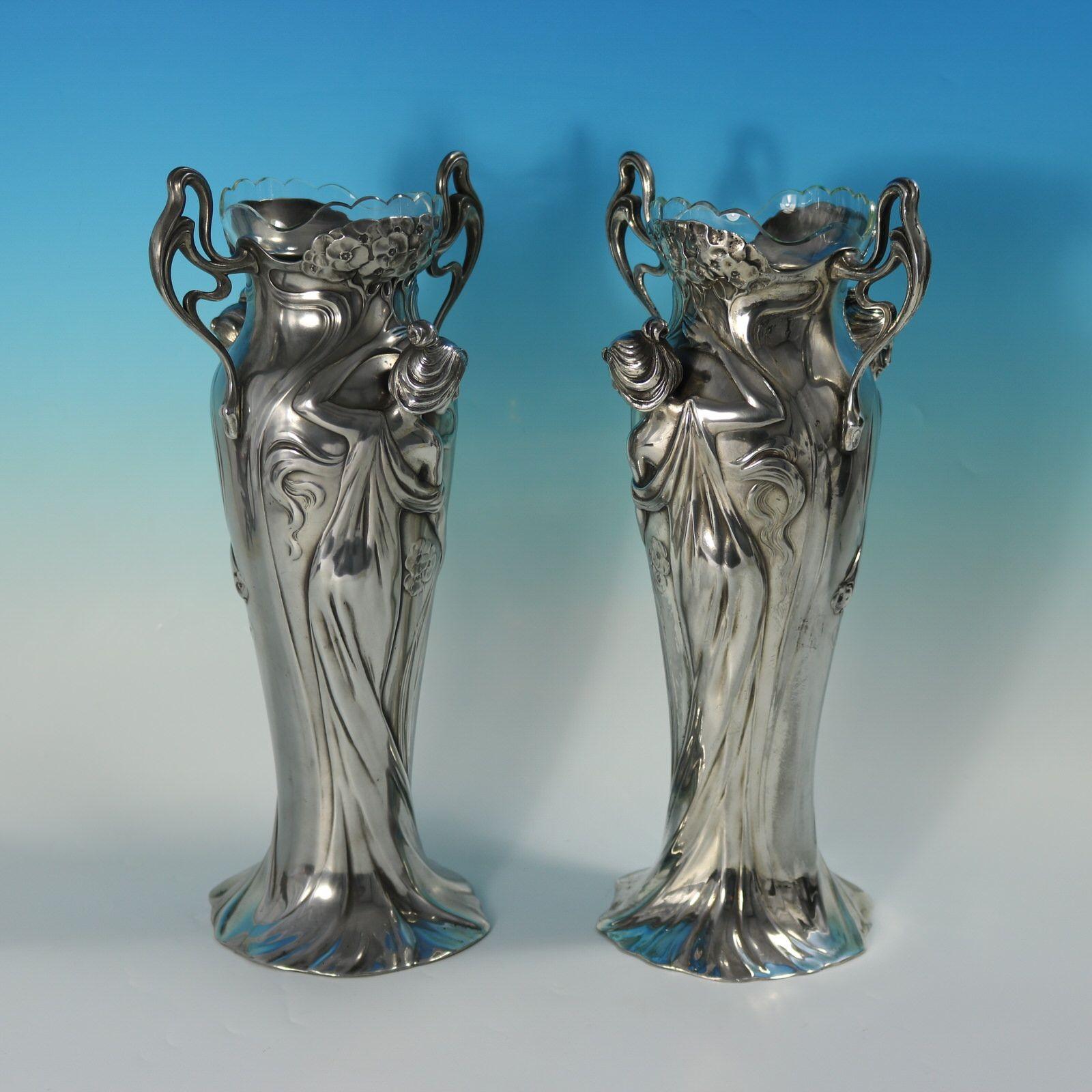 Coppia di vasi a due manici in stile Art Nouveau WMF, con fanciulle che indossano abiti fluenti. La parte inferiore del vestito forma la base. Dalla base spunta un albero fiorito. Completo di rivestimenti in vetro. I marchi del produttore includono