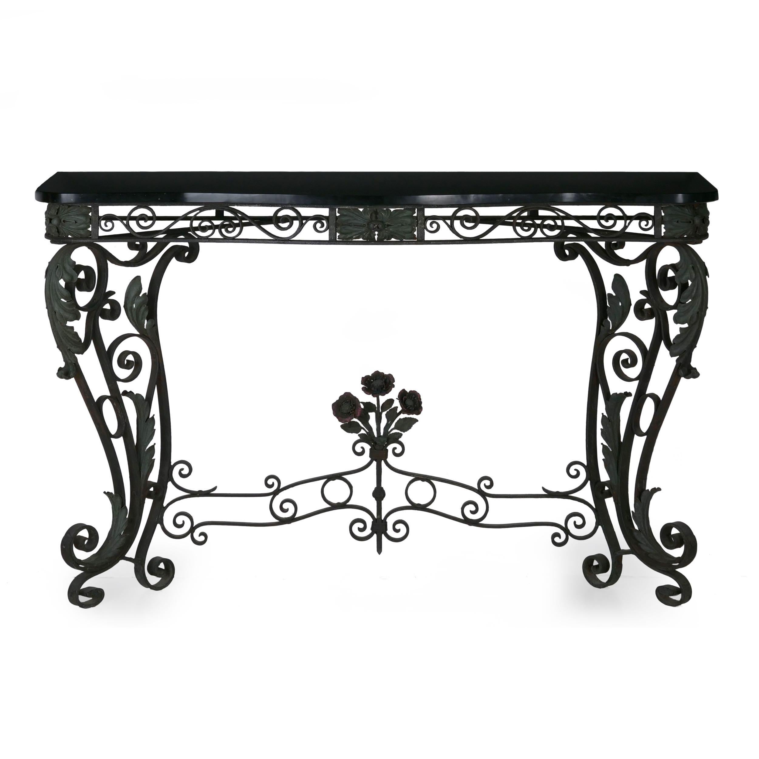 An attractive pair of perfectly matched early 20th century wrought iron console tables topped by polished black stone tops, each is delightfully decorated with pierced scrolling ironwork throughout the frame and legs intermingled with furls of