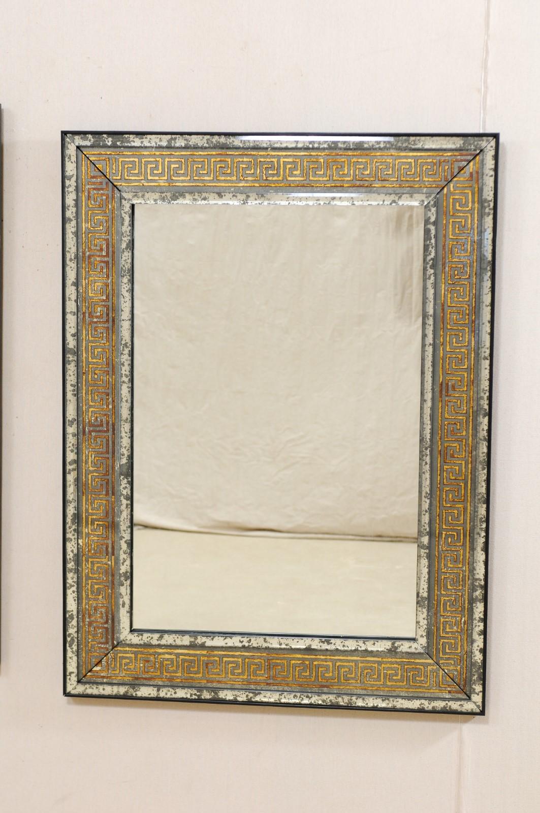 A pair of artisan made Greek key mirrors. This nice sized pair of rectangular-shaped mirrors Stand approximately just over 4 feet in height. They are artisan made with clean, antiqued-mirror inner and outer surrounds, with a gold verre églomisé