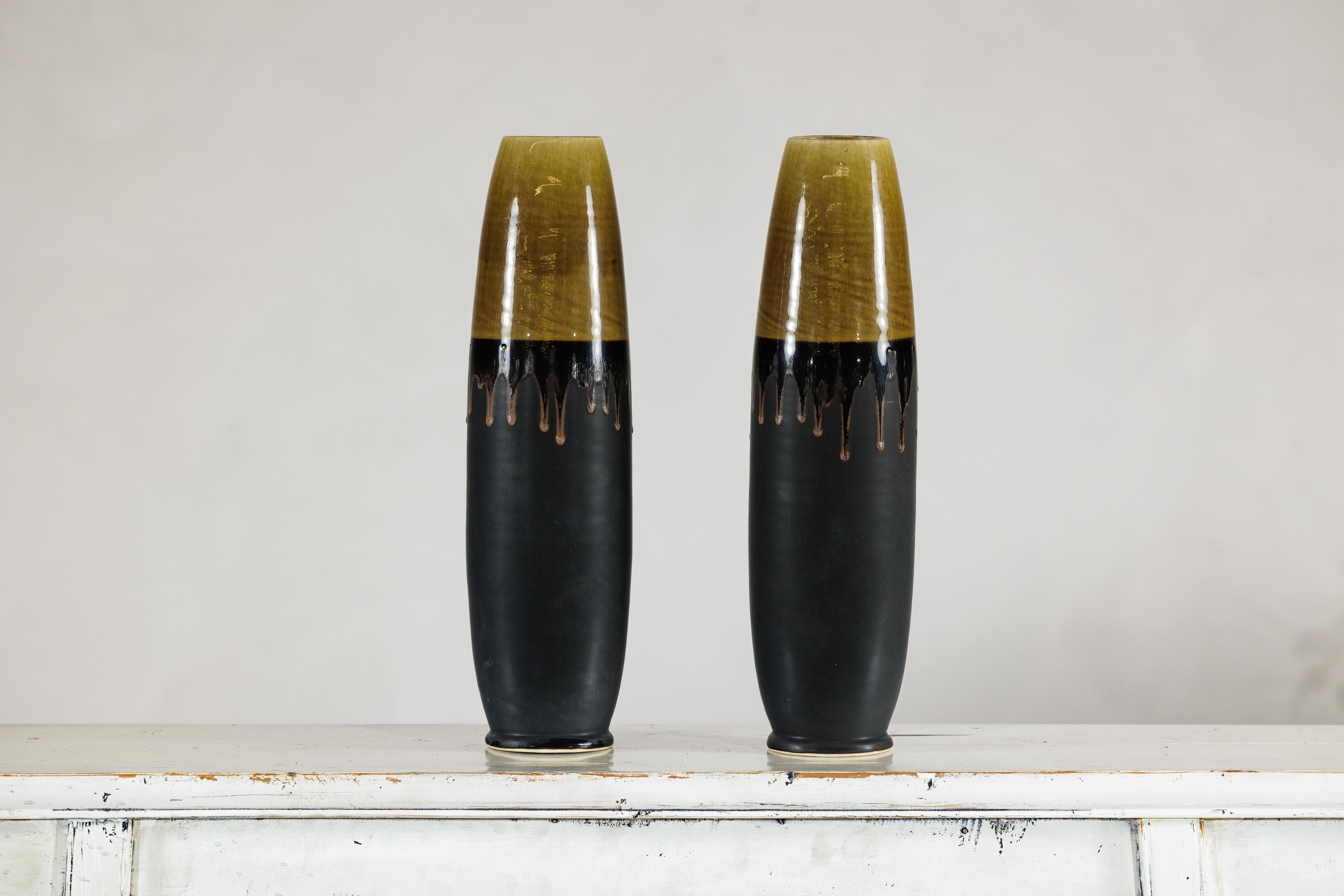 Questa coppia di vasi alti in ceramica artigianale ha una silhouette pulita e architettonica che si adatta a interni contemporanei ed eclettici. Ogni vaso è realizzato a mano con un corpo cilindrico sottile e un collo dolcemente affusolato, creando