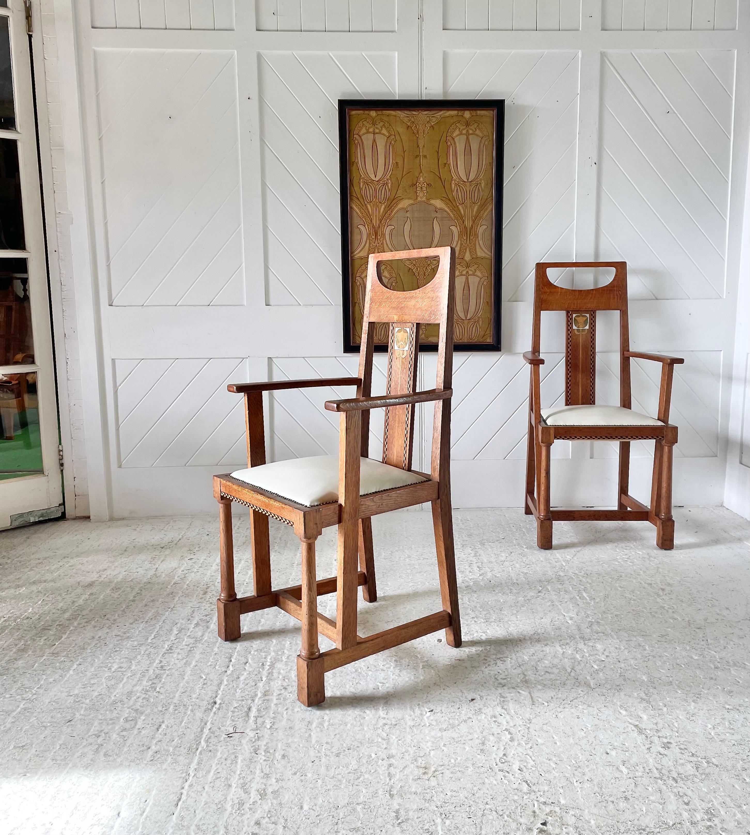 A pair of carver chairs in oak with decorative stylised flower inlay of pewter and green stained veneer with chequered pattern design, Seats in white Leather with brass upholstery studs.

Designed by G M Ellwood for J S Henry

Circa 1900

Exhibited