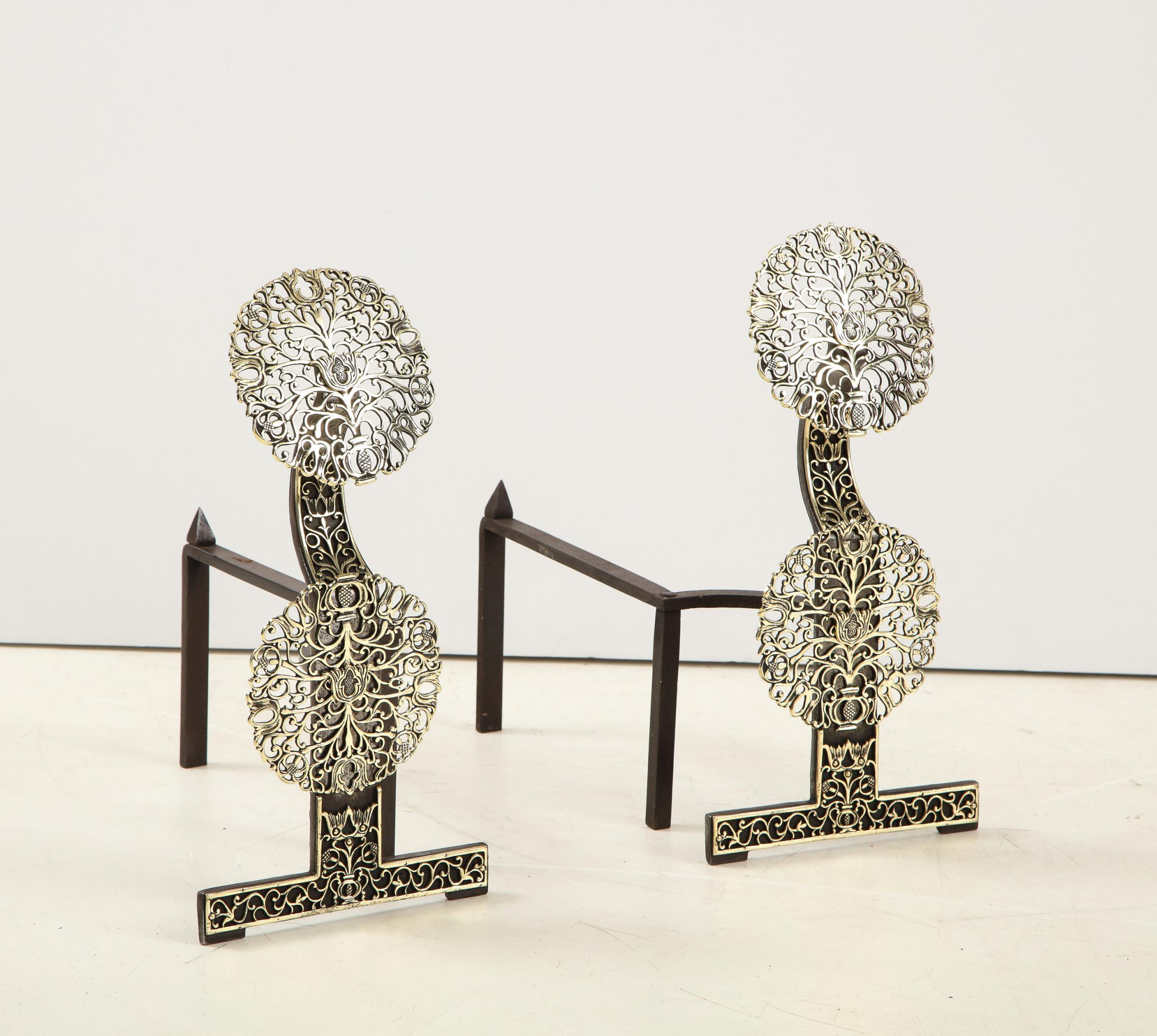 Fine pair of English Arts and Crafts mixed metal andirons in the manner of Ernest Gimson, having pierced brass bosses depicting vines and flower heads, on shaped wrought iron shafts and standing on 