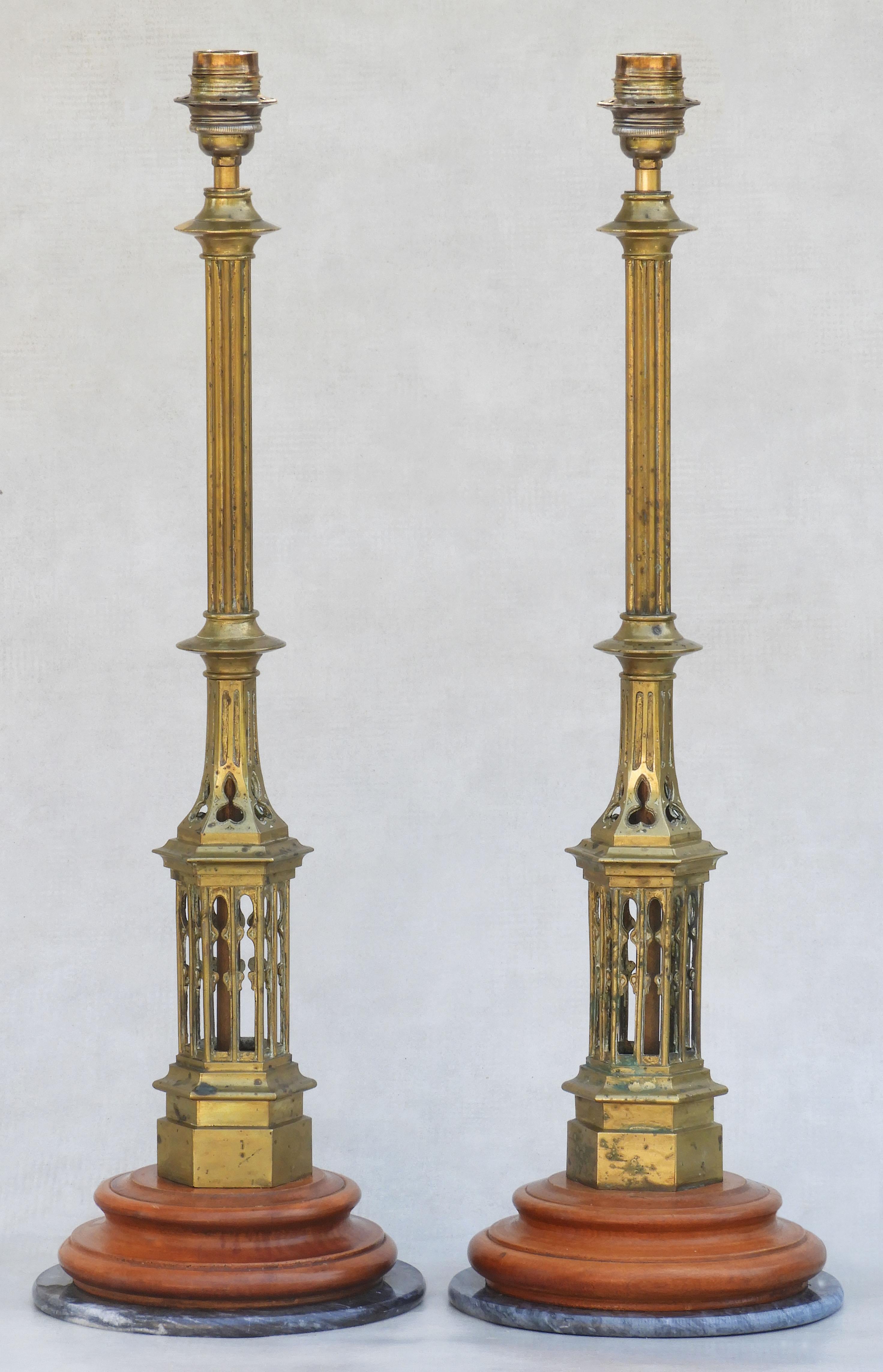A duo of tall, brass, Arts and Crafts lamps.  An unusual pair of Neo-Gothic architectural elements, later mounted on wood and marble plinths and converted to tabletop lighting.  In good antique condition with nice patina, clean but not