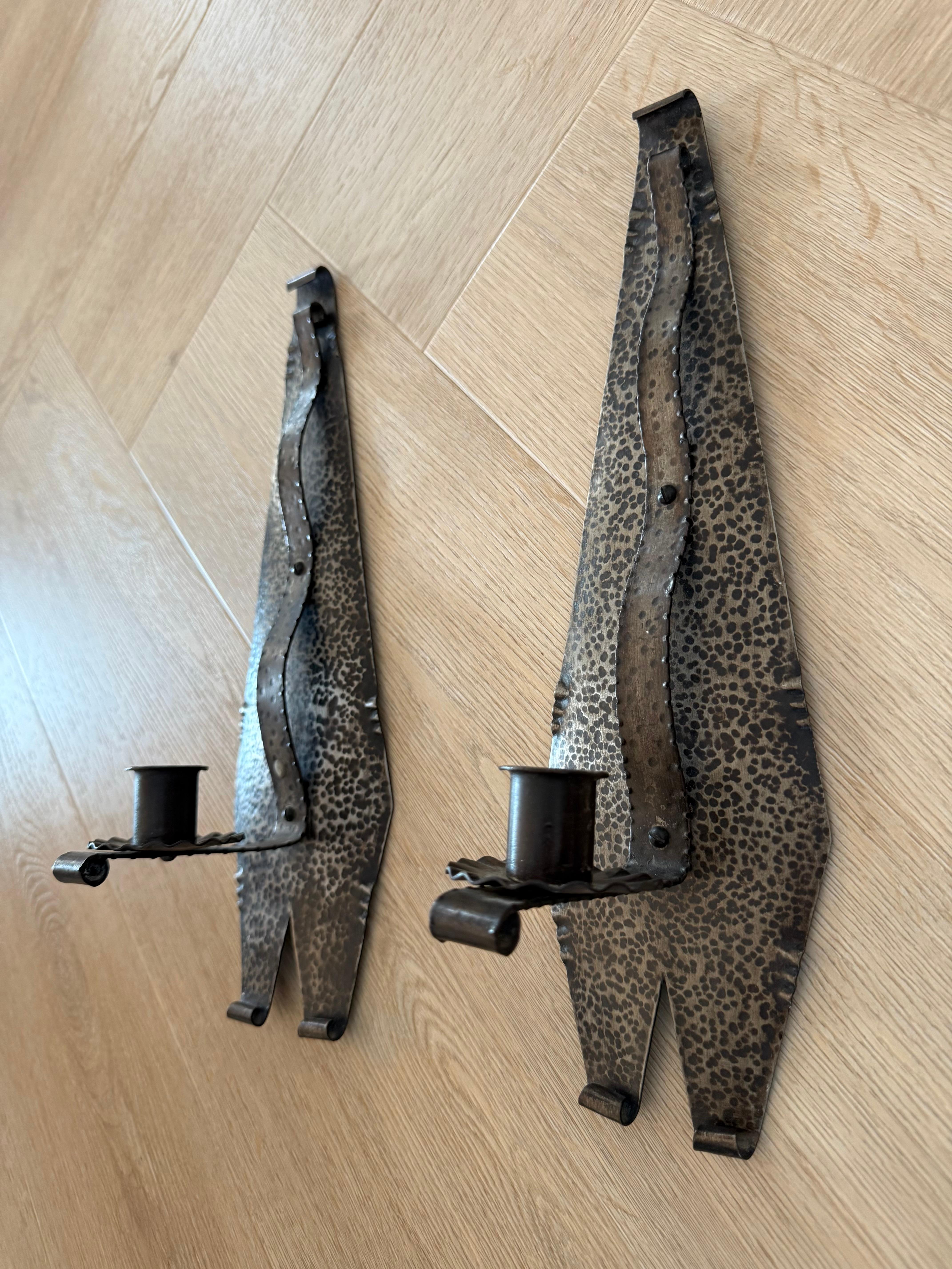 An elegant and stylish pair of Arts & Crafts wall candlesticks.

These beautifully hand-forged and hand-hammered wrought iron sconces exude craftsmanship and timeless design. Their elongated, geometric backplates feature a striking hammered surface,