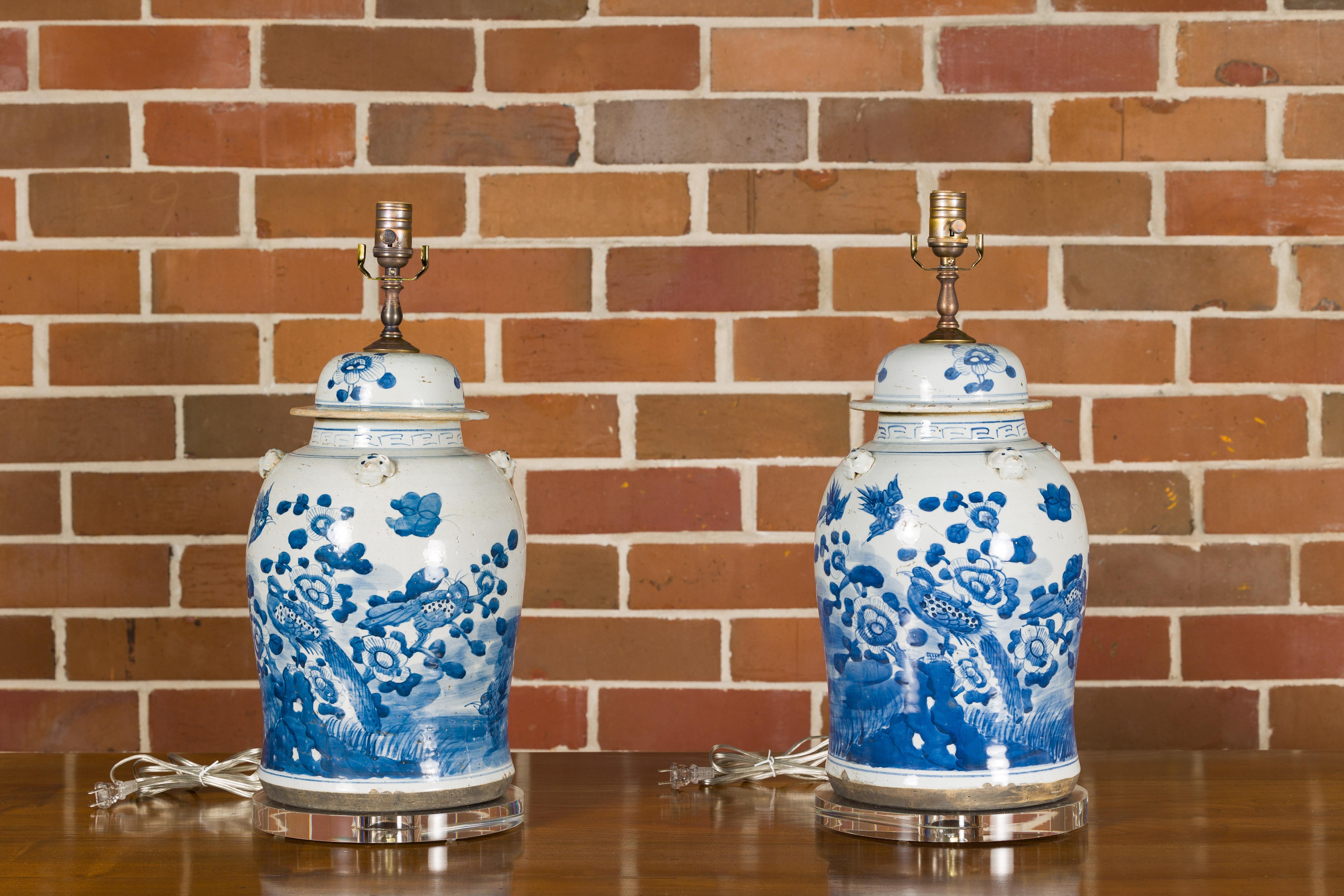 A pair of Asian porcelain jars with blue and white floral and bird décor, newly mounted as table lamps on lucite bases. This pair of Asian porcelain jars has been thoughtfully repurposed into stunning modern table lamps, fusing timeless elegance