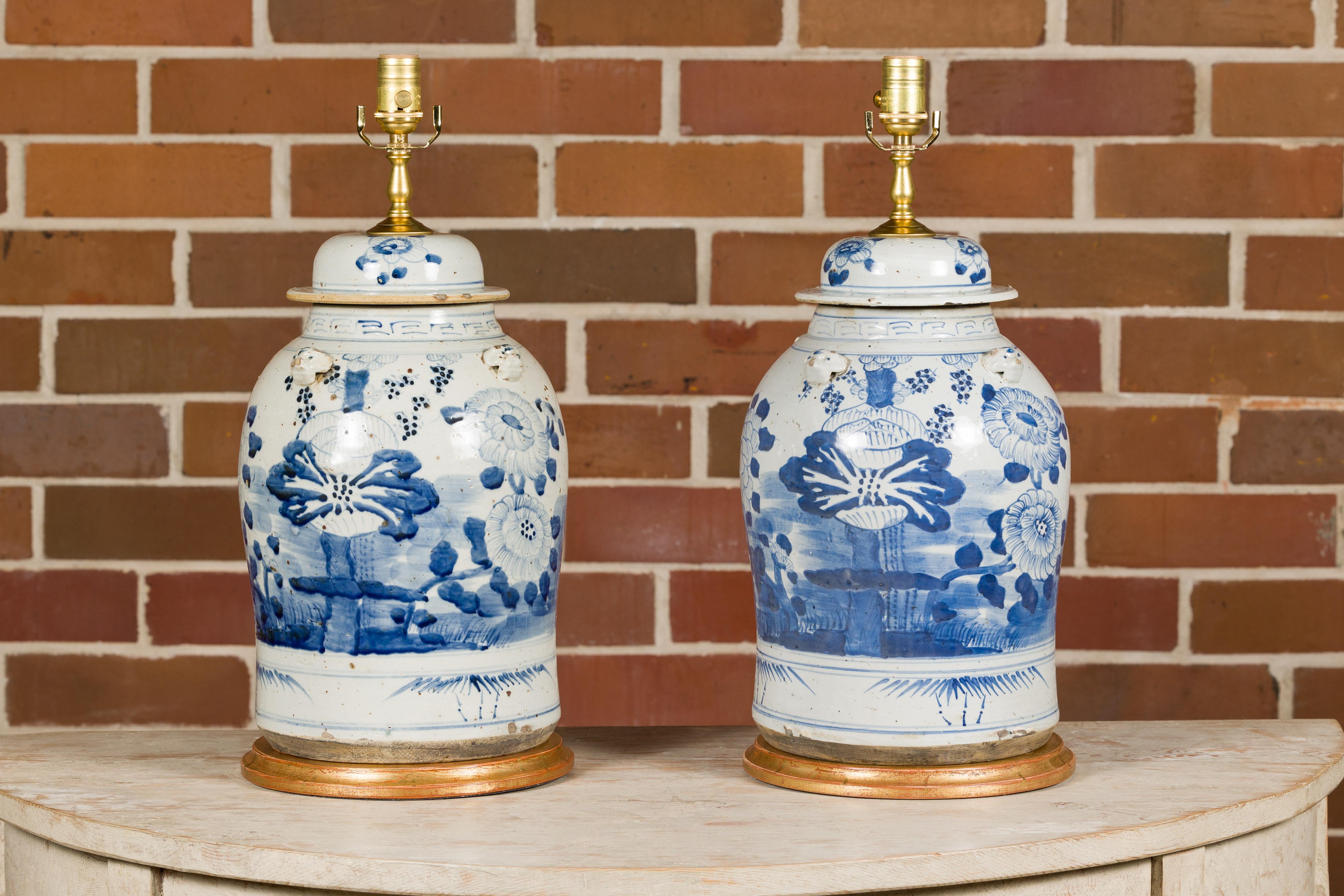 A pair of Asian porcelain jars with blue and white floral décor, newly mounted as table lamps on circular gilded bases. Embrace the captivating beauty of Eastern artistry with this exquisite pair of Asian porcelain jars, transformed into table lamps