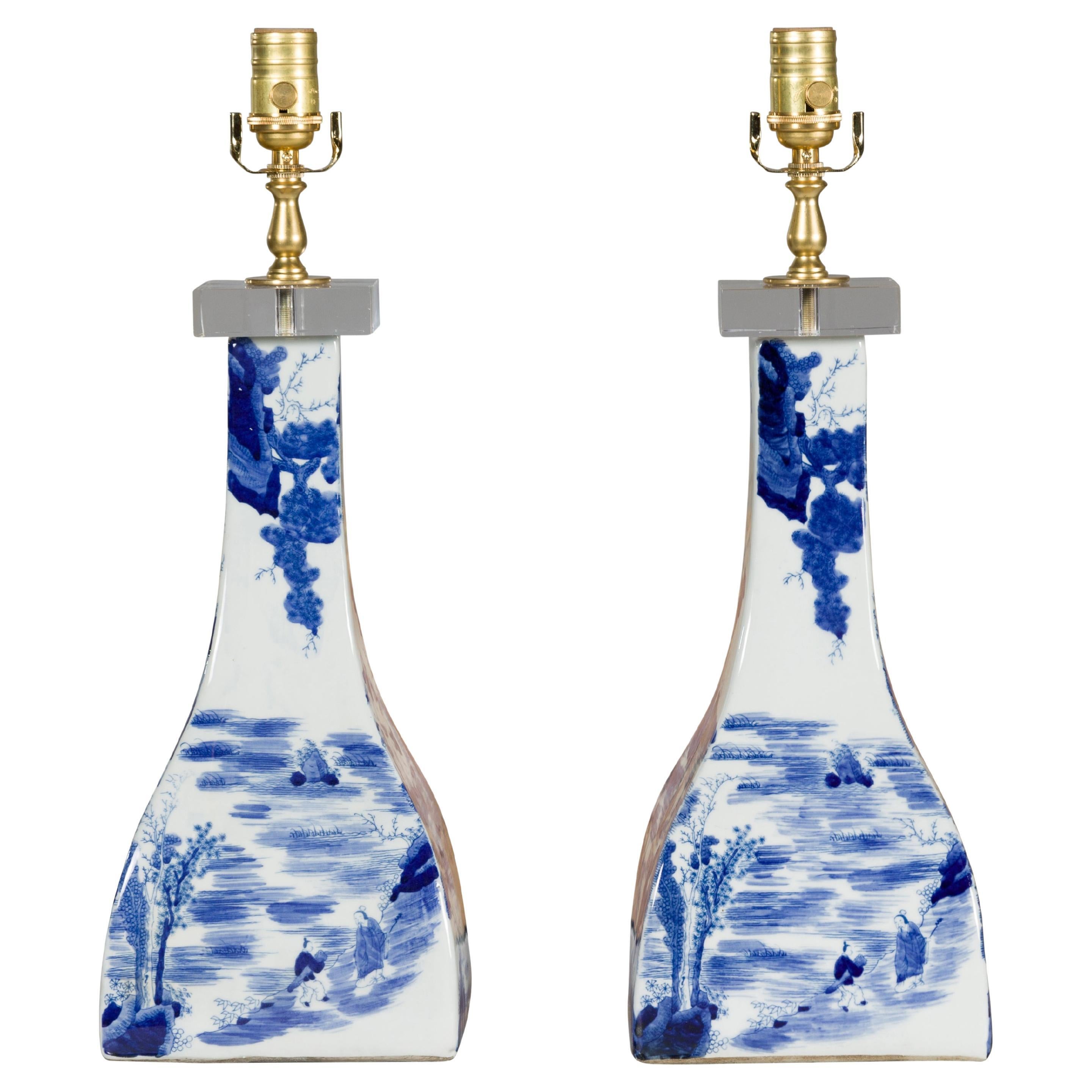 A pair of Asian blue and white porcelain table lamps mounted on custom lucite bases. Introducing a resplendent pair of Asian blue and white porcelain table lamps, masterfully mounted on custom lucite bases that effortlessly merge traditional