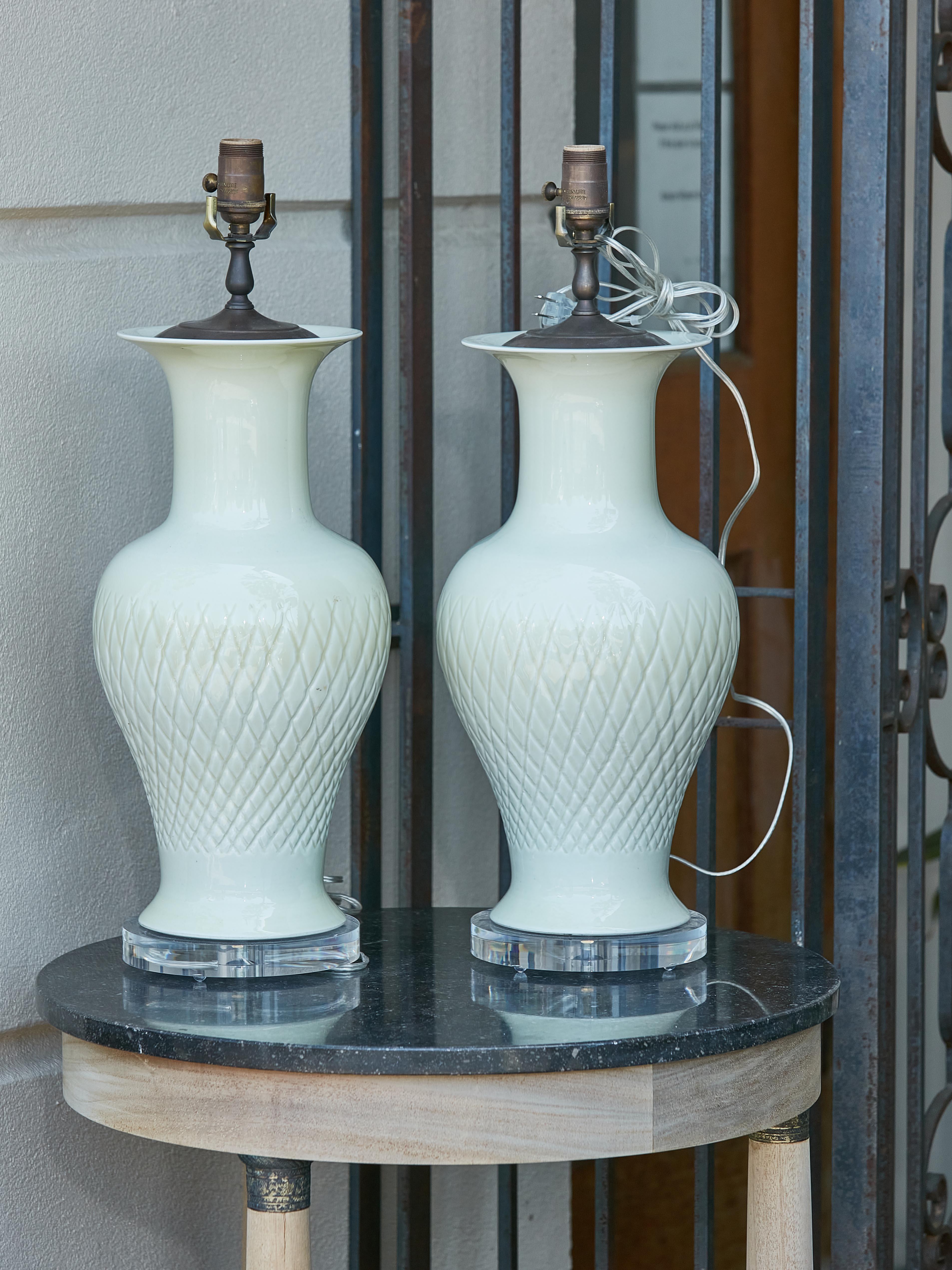 A pair of Asian celadon single light table lamps with cross hatched décor on the belly, mounted on circular lucite bases and rewired for the USA. Infuse your interior space with an aura of ethereal grace and classic allure with this enchanting pair