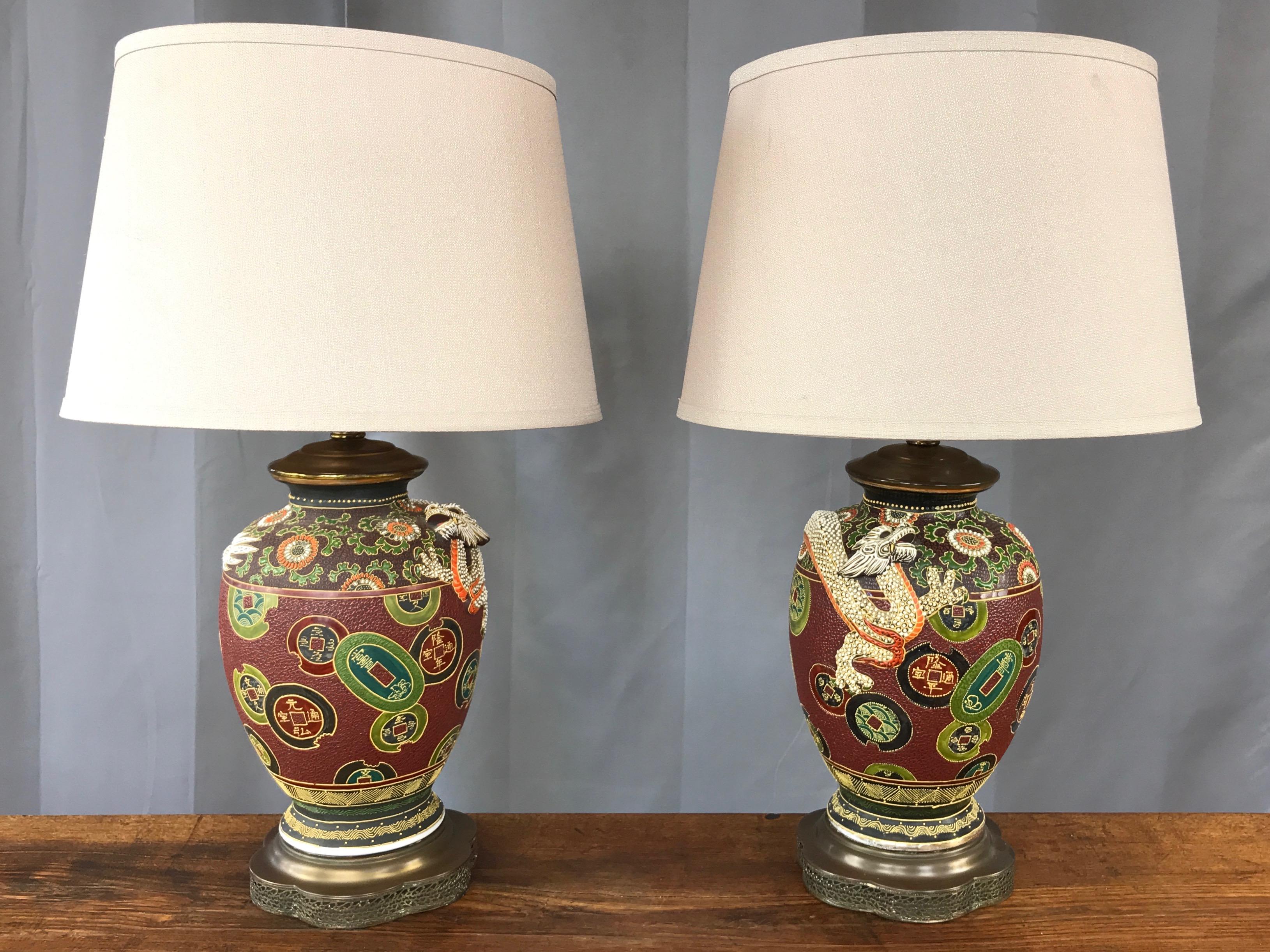 A pair of Japanese midcentury Chinese-style dragon and charm motif hand-decorated ceramic table lamps with pierced brass bases.

Ginger jar form encircled by a white dragon sculpted in exceptionally lively relief. Charms and coins are scattered