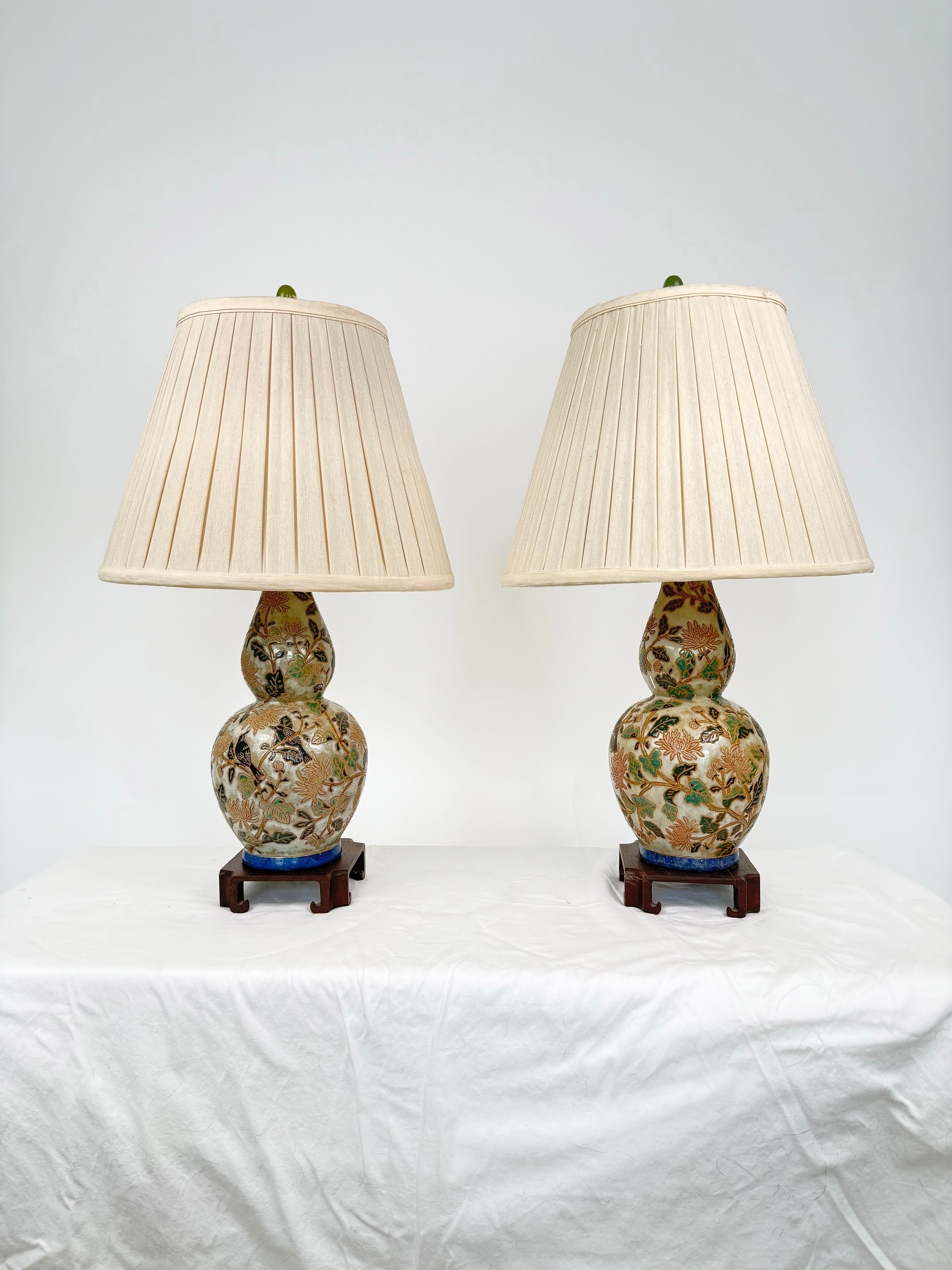 Paire de lampes gourdes asiatiques en céramique montées sur des bases en bois avec de beaux abat-jours en soie et des fleurons en jade.  Les lampes présentent une scène de jardin en relief pressé de chrysanthèmes, d'oiseaux et de feuilles avec de