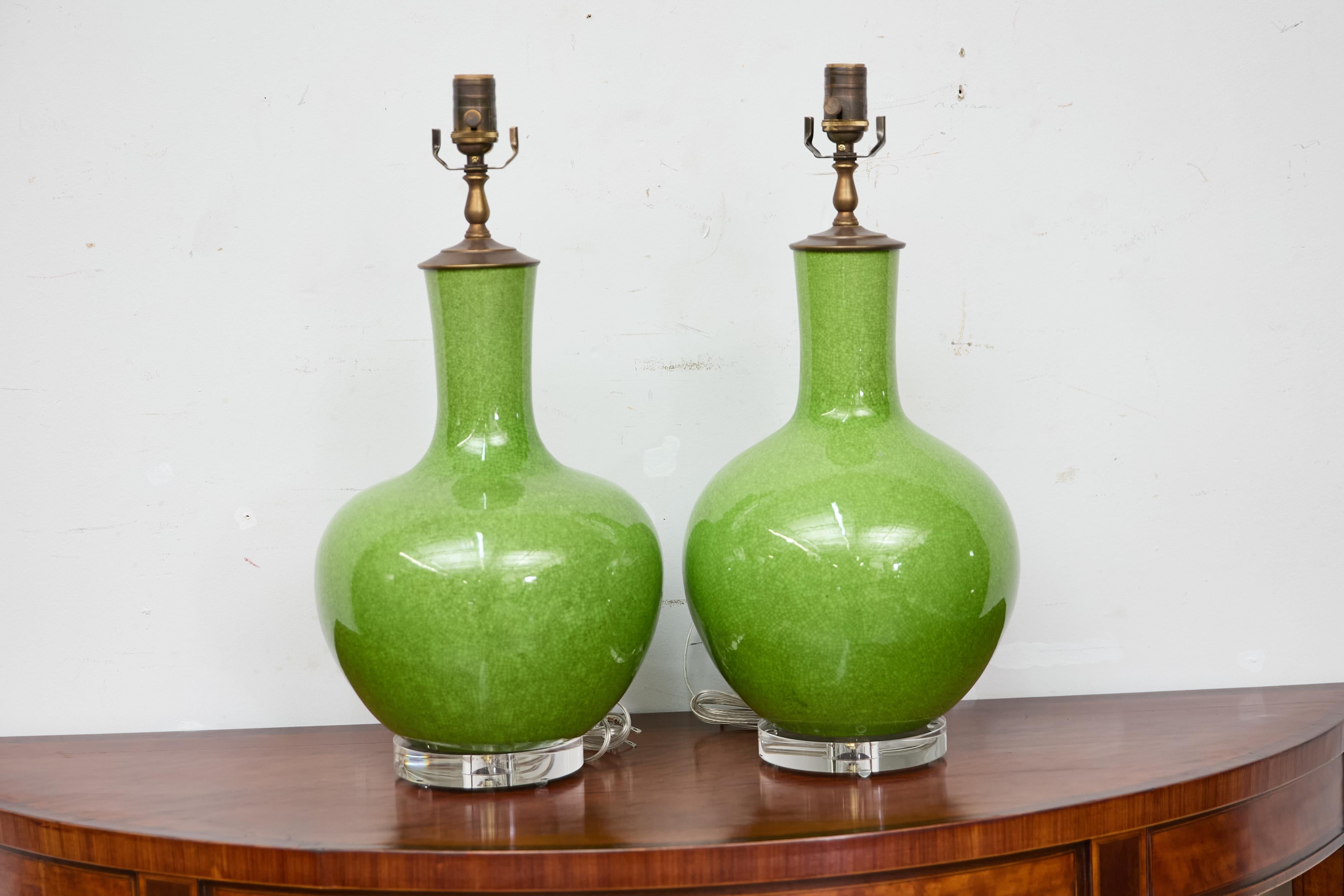 Una coppia audace ed elegante di lampade da tavolo in porcellana verde brillante, ciascuna realizzata con una forma di vaso a collo dritto con una caratteristica smaltatura a crepe. La vibrante finitura verde è ricca e satura, mentre la fine