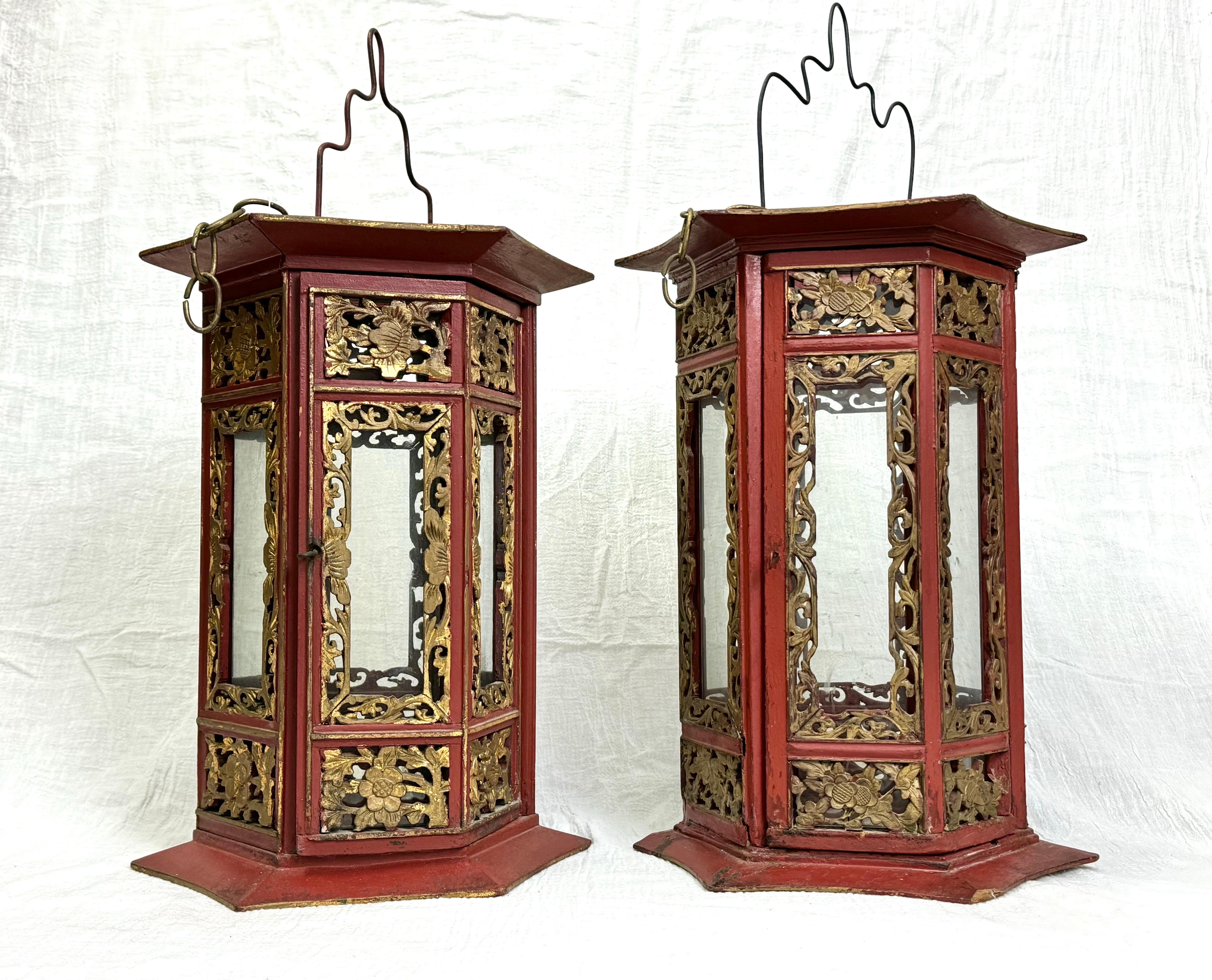Pair of Asian Hand Carved Wooden Lanterns. Nice decorative pair in a rich cinnabar color. This pair is not identical but very similar. Heavily carved gilt wood with amazing detail. Hinged glass doors open to insert a large candle. Iron handles to
