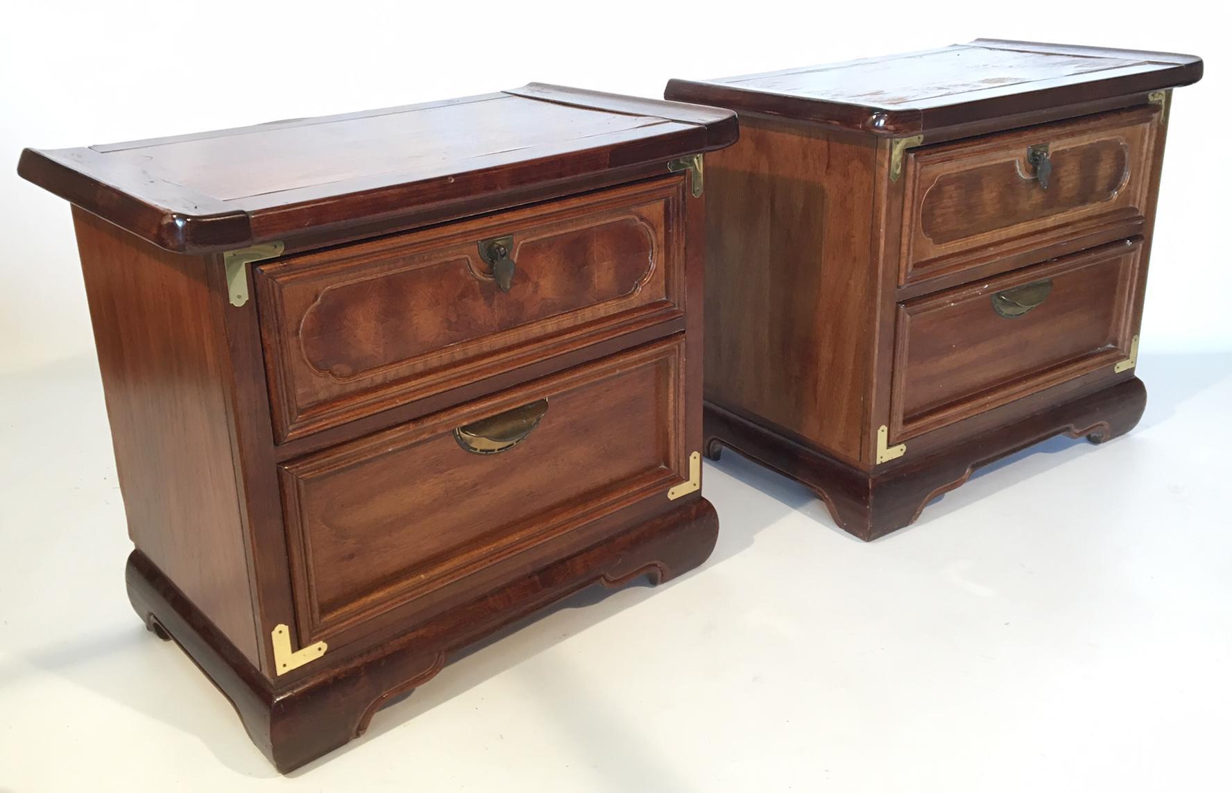 Pair of heavy wood nightstands in an Asian chinoiserie style feature campaign style brass hardware and detailing and Ming style legs. Excellent structural condition, finish shows wear, especially on top surface.