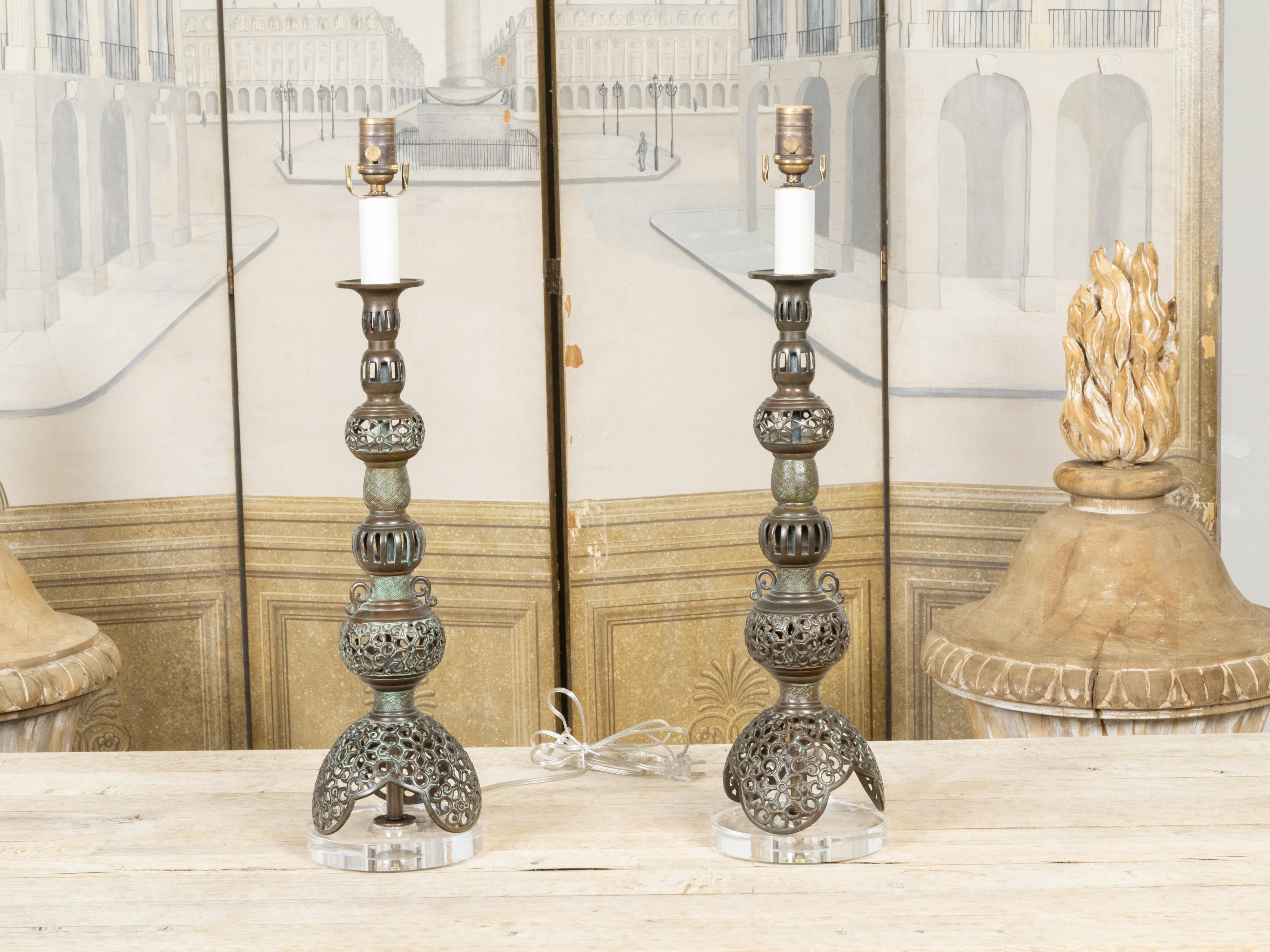A pair of Asian bronze table lamps from the mid-20th century, with openwork décor, single lights and custom lucite bases, wired for the USA. Created in Asia during the Midcentury period, each of this pair of bronze table lamps features an elegant