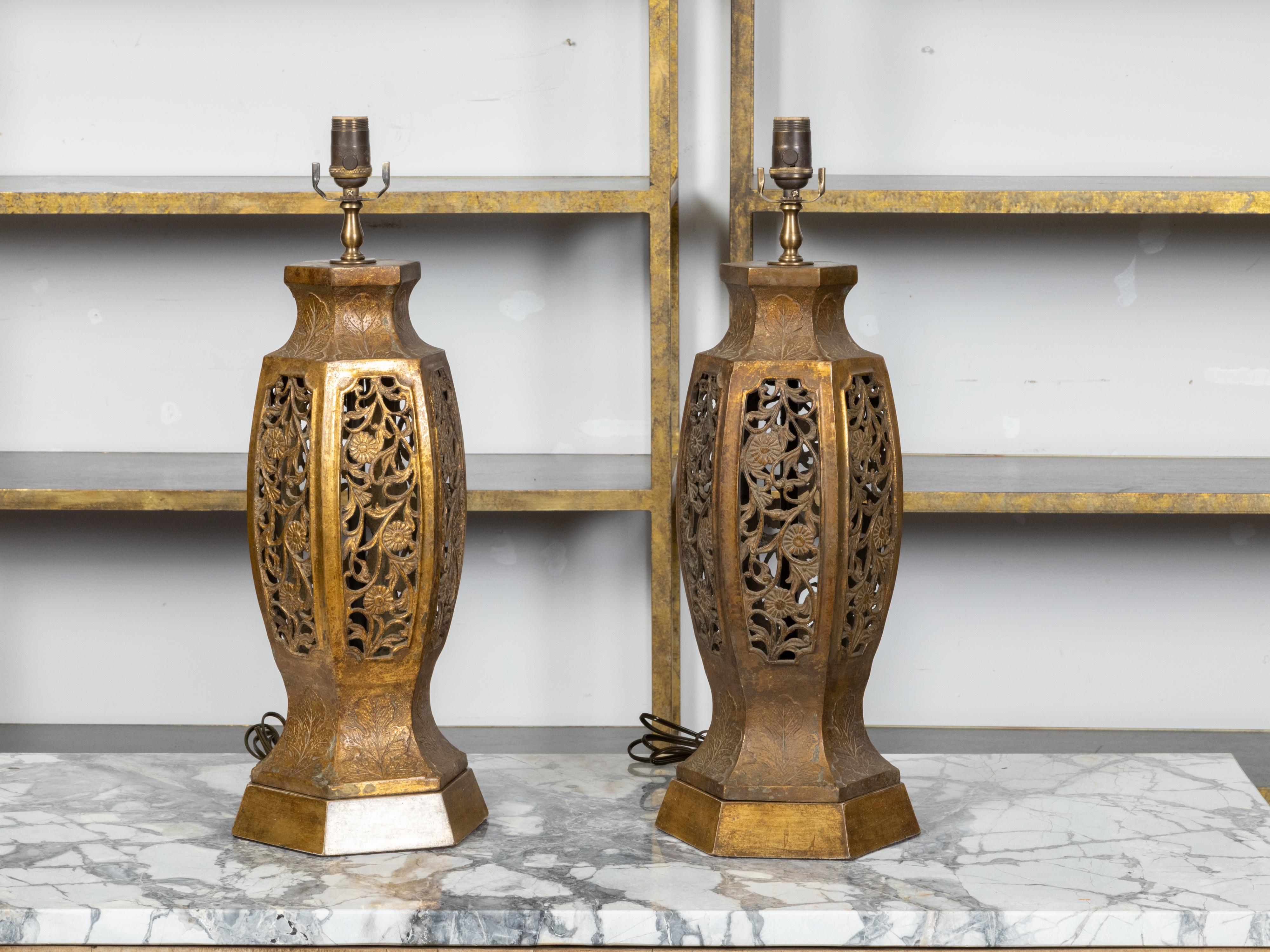 A pair of vintage Asian carved table lamps from the mid 20th century with pierced openwork foliage and floral motifs, resting on hexagonal bases. Created in Asia during the Midcentury period, each of this pair of table lamps attracts our attention