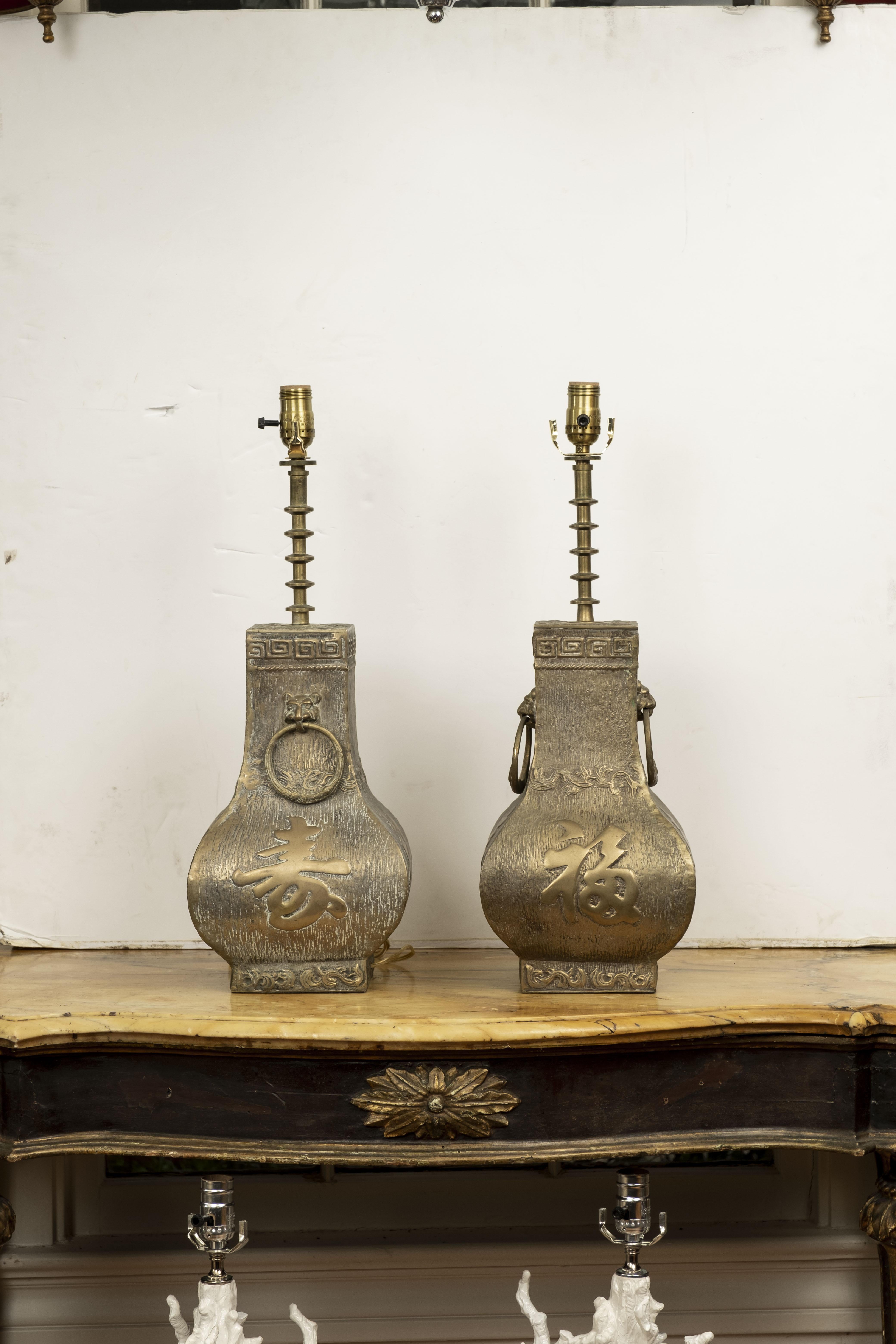 Pair of Asian Modern brass lamps by James Mont. These stunning heavyweight Hollywood Regency brass lamps feature Chinese characters, Greek keys and lion heads handles. This great pair of midcentury brass lamps have been newly wired with new sockets
