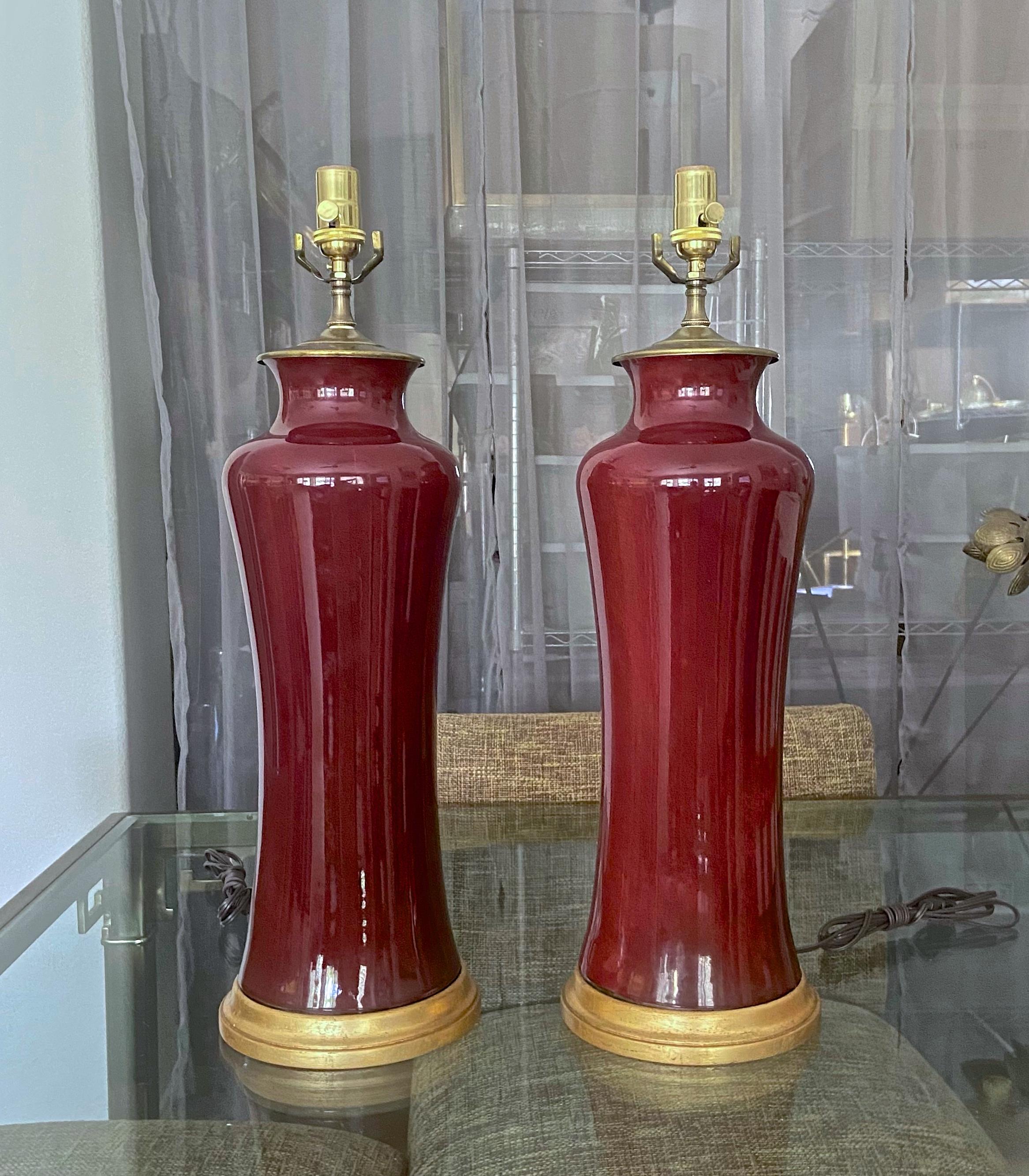 Pair of tall Chinese oxblood porcelain vases mounted on gilt turned wood lamp bases. Complimented with antiqued brass finish fittings. Rewired with new 3 way sockets and brown cords . Overall height top of socket 25