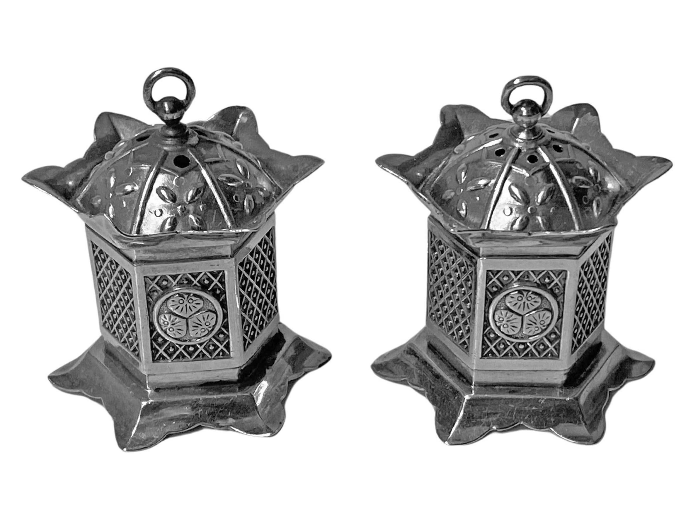 Pair of Asian Silver casters C.1930. Each of hexagonal shape and a surround of panels, some depicting lotus. Dome pierced tops allowing for salt and pepper respectively. The bases have opening slides to fill with salt and pepper. Each stamped