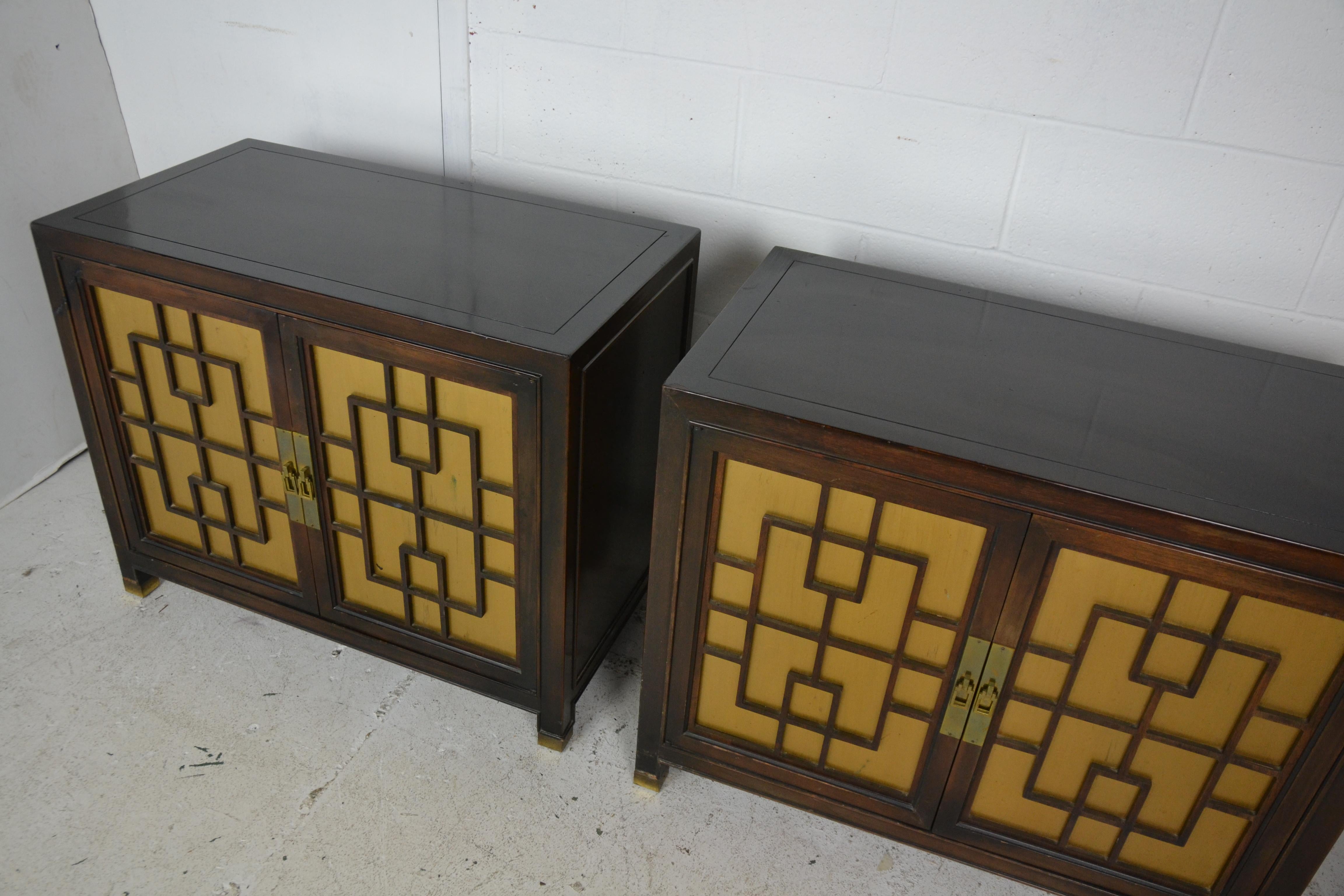 A pair of Chinese hardwood end tables or nightstands with traditional Chinese fretwork over gold painted panel doors. Brass toe caps and escutcheons.