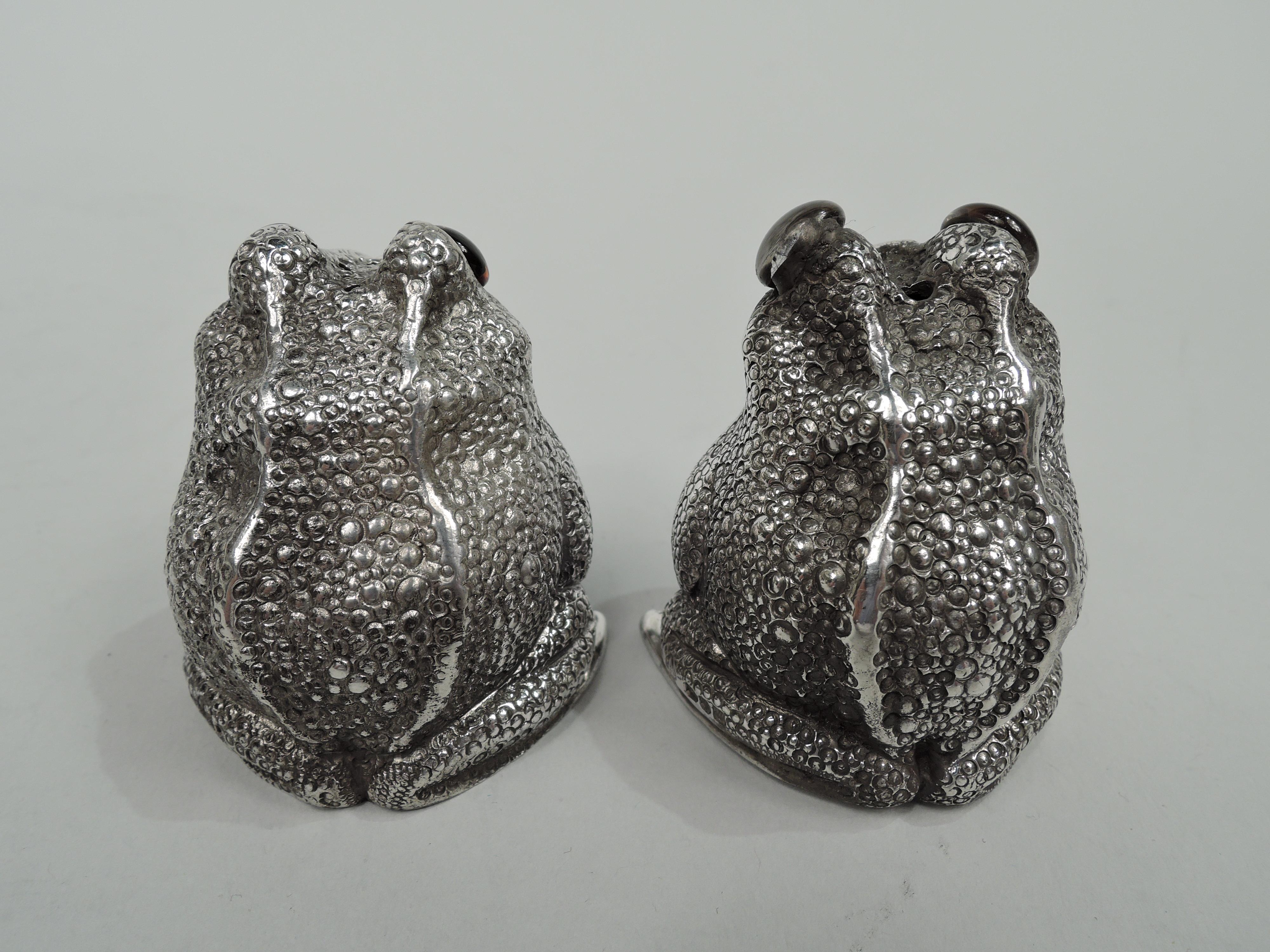 Pair of Elizabeth II sterling silver figural frog salt and pepper shakers. Made by Asprey in London in 1967-8. Each: A squatting, smirking reptile with glass exophthalmic eyes, and scaly back. Head top pierced. Underside has plastic plug. Fully