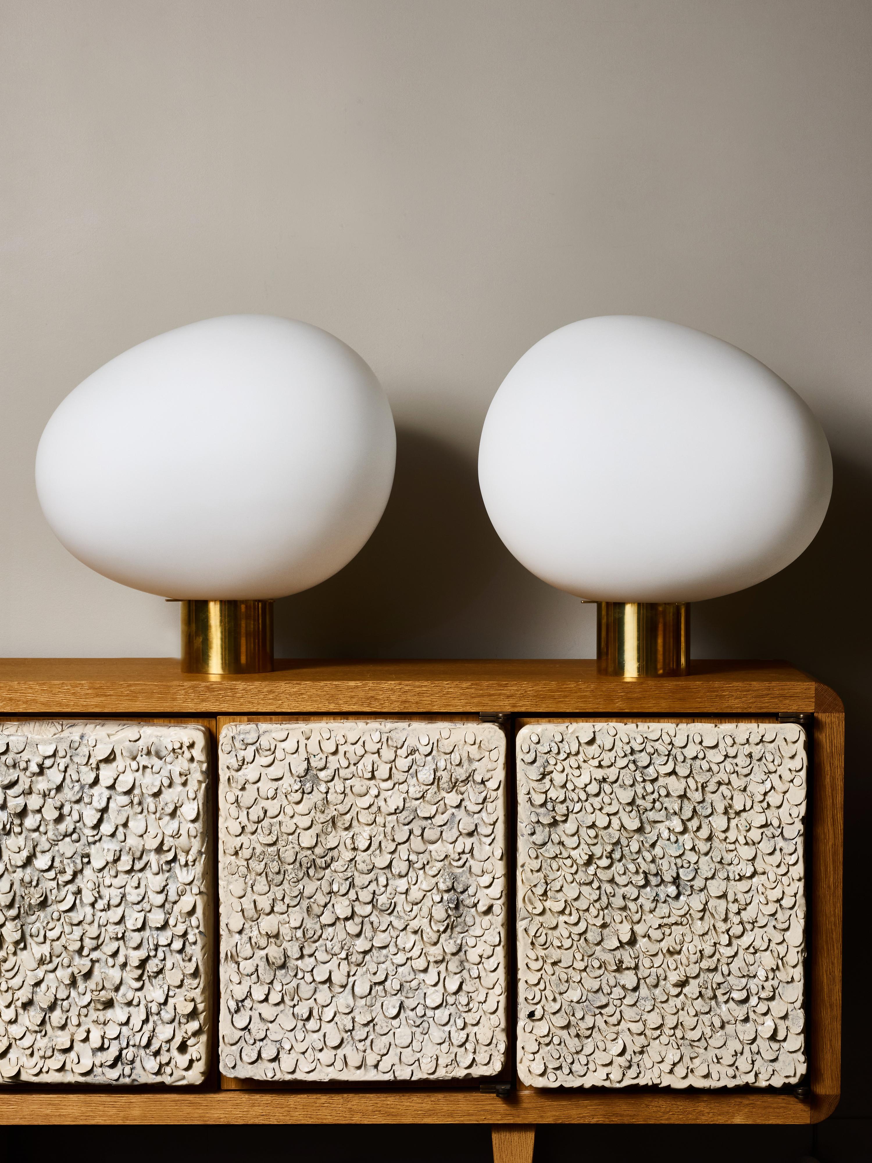 Llamativa pareja de lámparas de sobremesa contemporáneas, cada una de ellas con una pantalla de cristal opalino de bella forma que descansa sobre una base cilíndrica de latón pulido que añade un refinado contraste. Sus siluetas orgánicas, parecidas