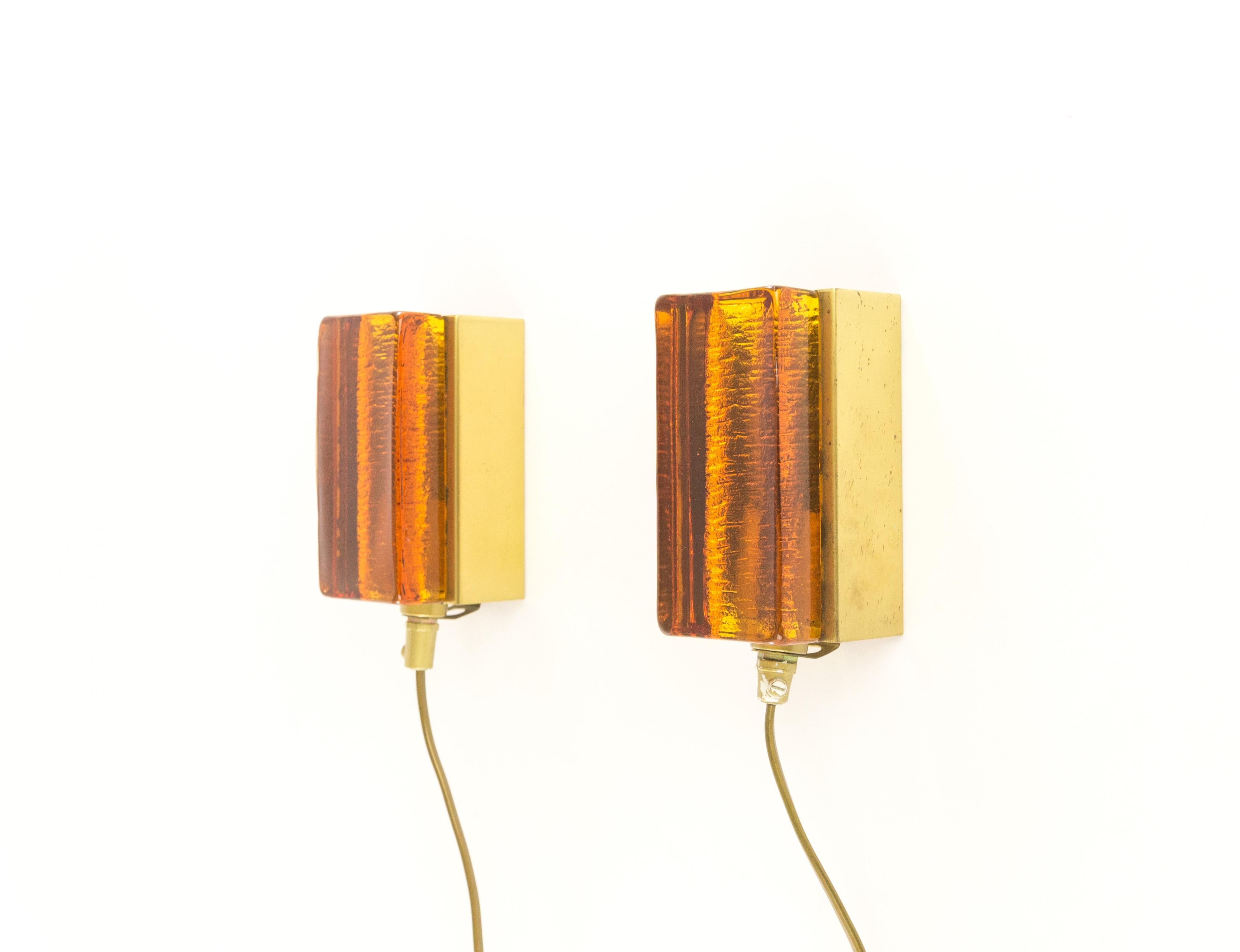 Un ensemble de deux appliques Atlantic en verre ambré et en laiton qui sont produites par le fabricant de luminaires danois Vitrika dans les années 1970. Les deux lampes sont composées de deux parties : un corps en verre massif fait à la main en or,