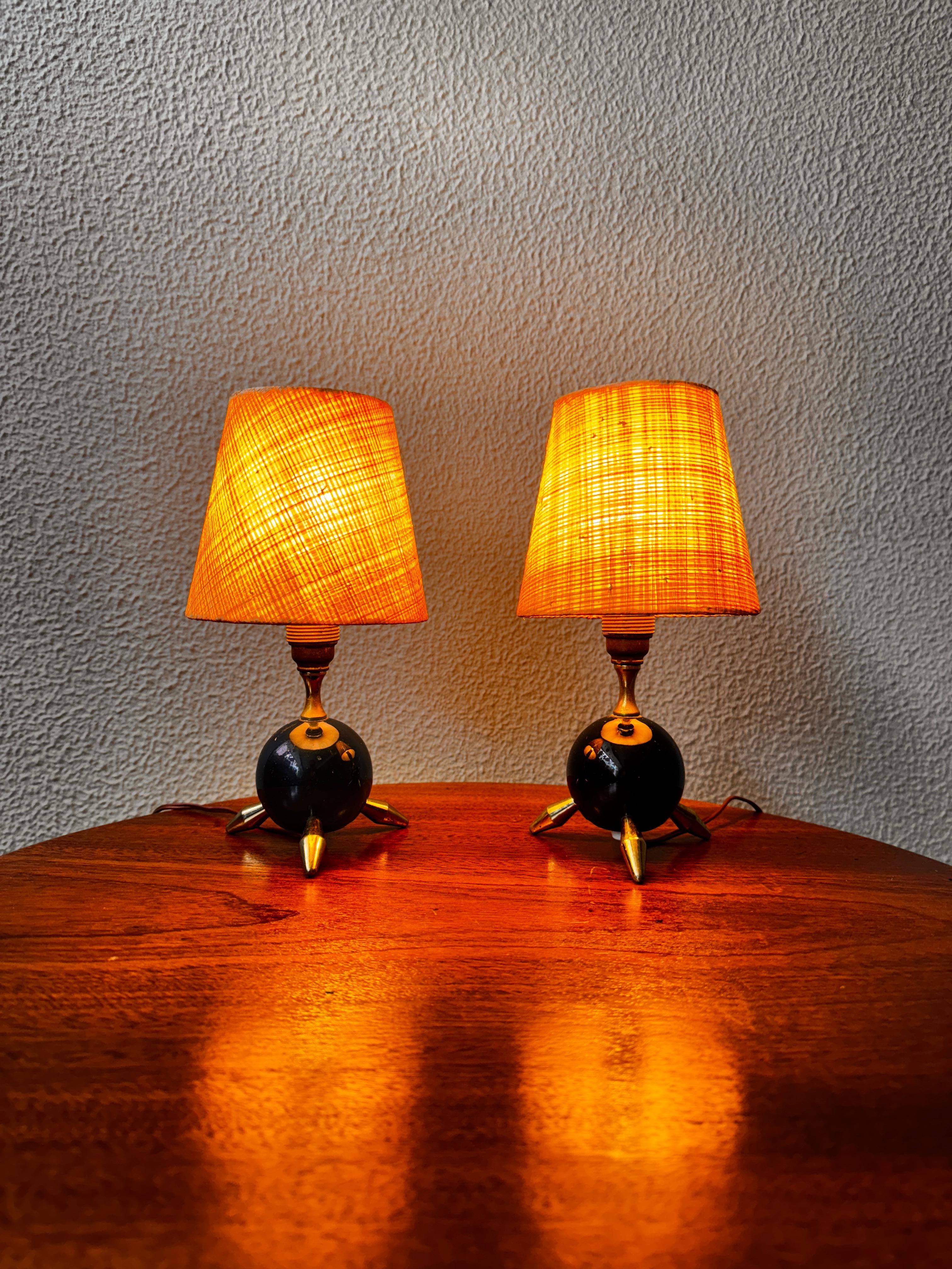 Affascinante coppia di lampade da tavolo a treppiede Atomic, Italia, anni '50. Queste miniature scultoree del futurismo di metà secolo incarnano lo spirito dell'era atomica con le loro silhouette giocose e spaziali. Le proporzioni compatte sono una