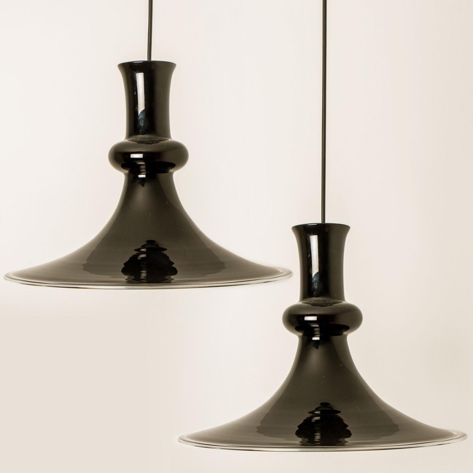 Questa coppia di bellissime lampade in vetro del marchio danese Holmegaard ha un bellissimo colore melanzana. Il design è opera di Michael Bang, un designer il cui lavoro è oggi molto ricercato dai collezionisti del marchio. Model Etude, una forma