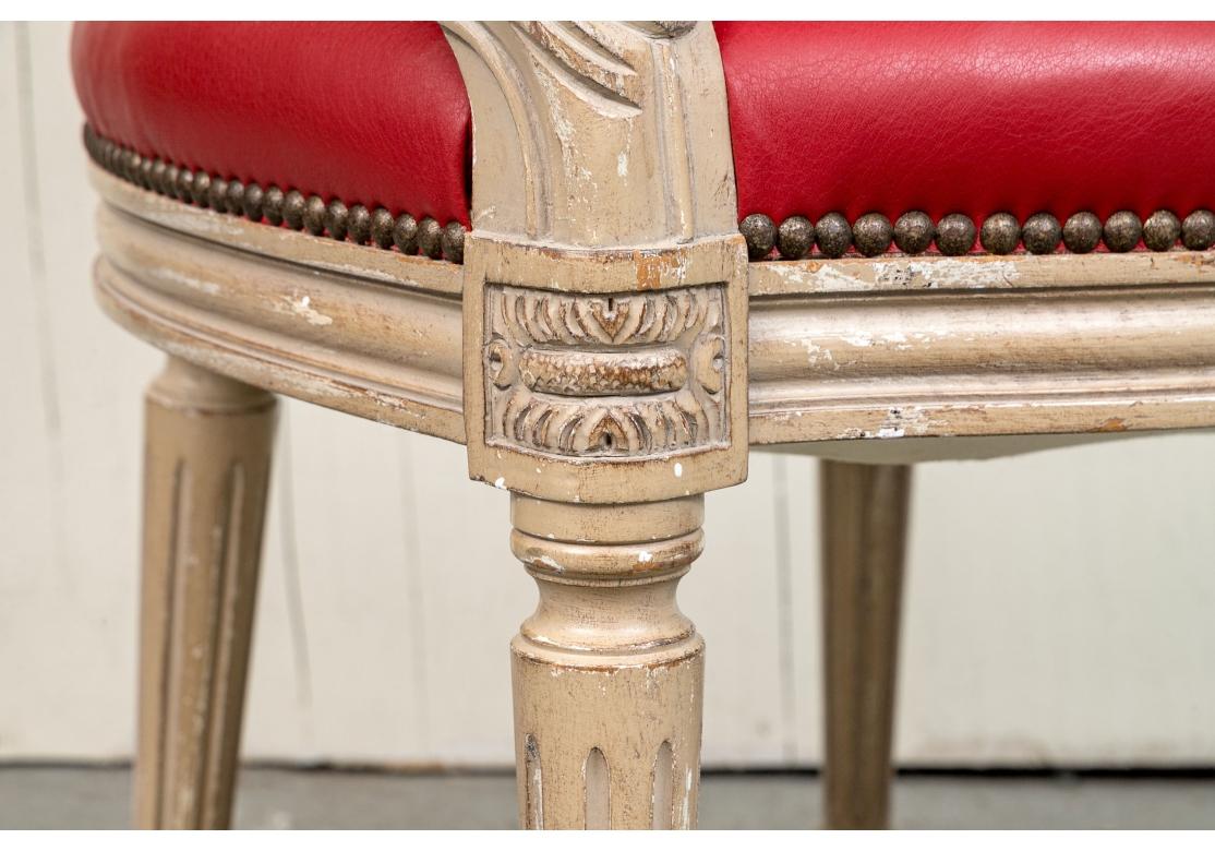Pair of fine quality fauteuils upholstered in faux red leather with brass tacks, leather manchettes and contrasting taffeta plaid fabric on verso. The distressed paint decorated frames with carved details, corner medallions and resting on fluted