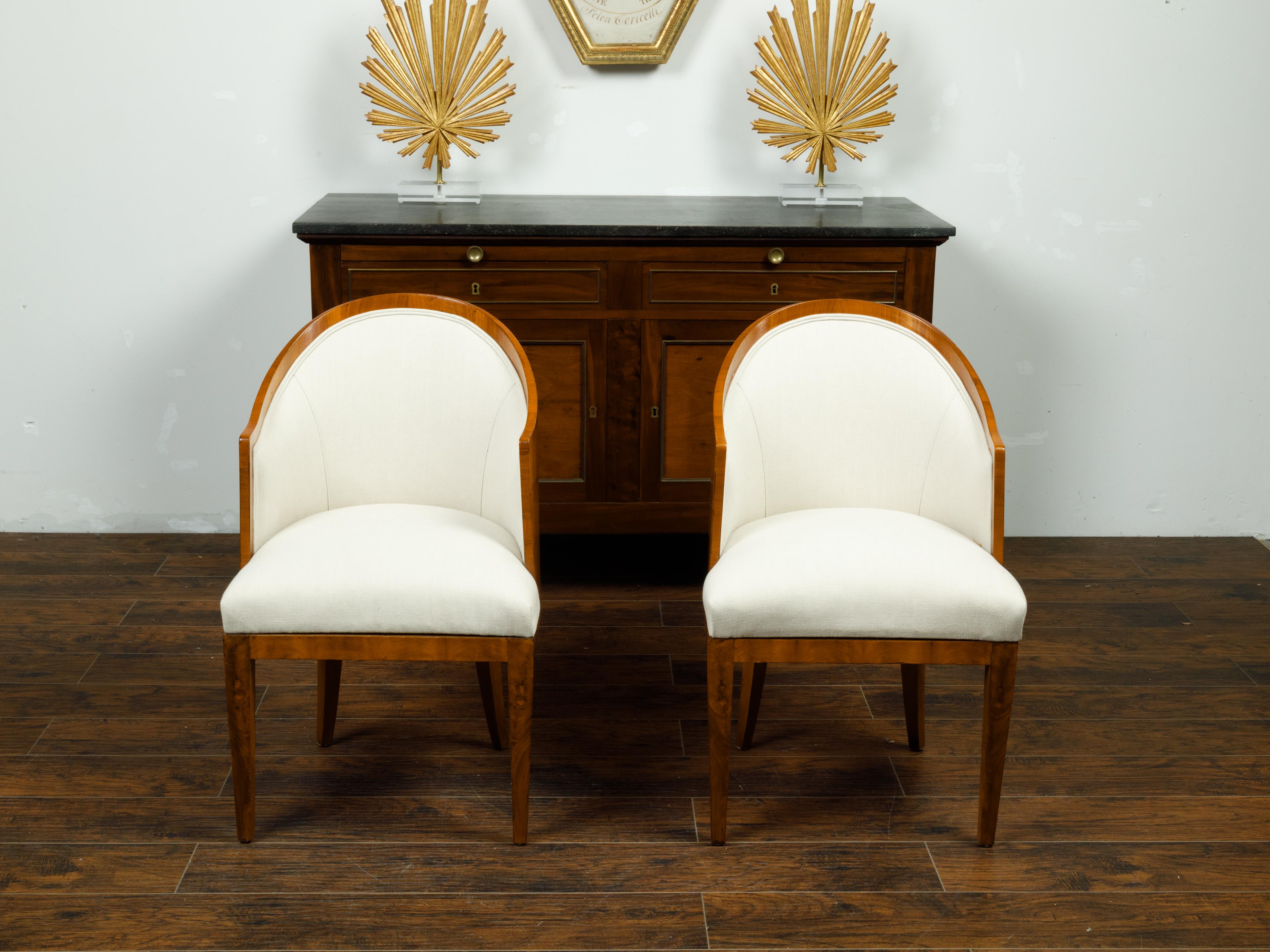 A pair of Austrian Biedermeier period walnut wraparound back armchairs from the mid 19th century, with tapered legs and new upholstery. Created in Austria during the second quarter of the 19th century, each of this pair of Biedermeier chairs