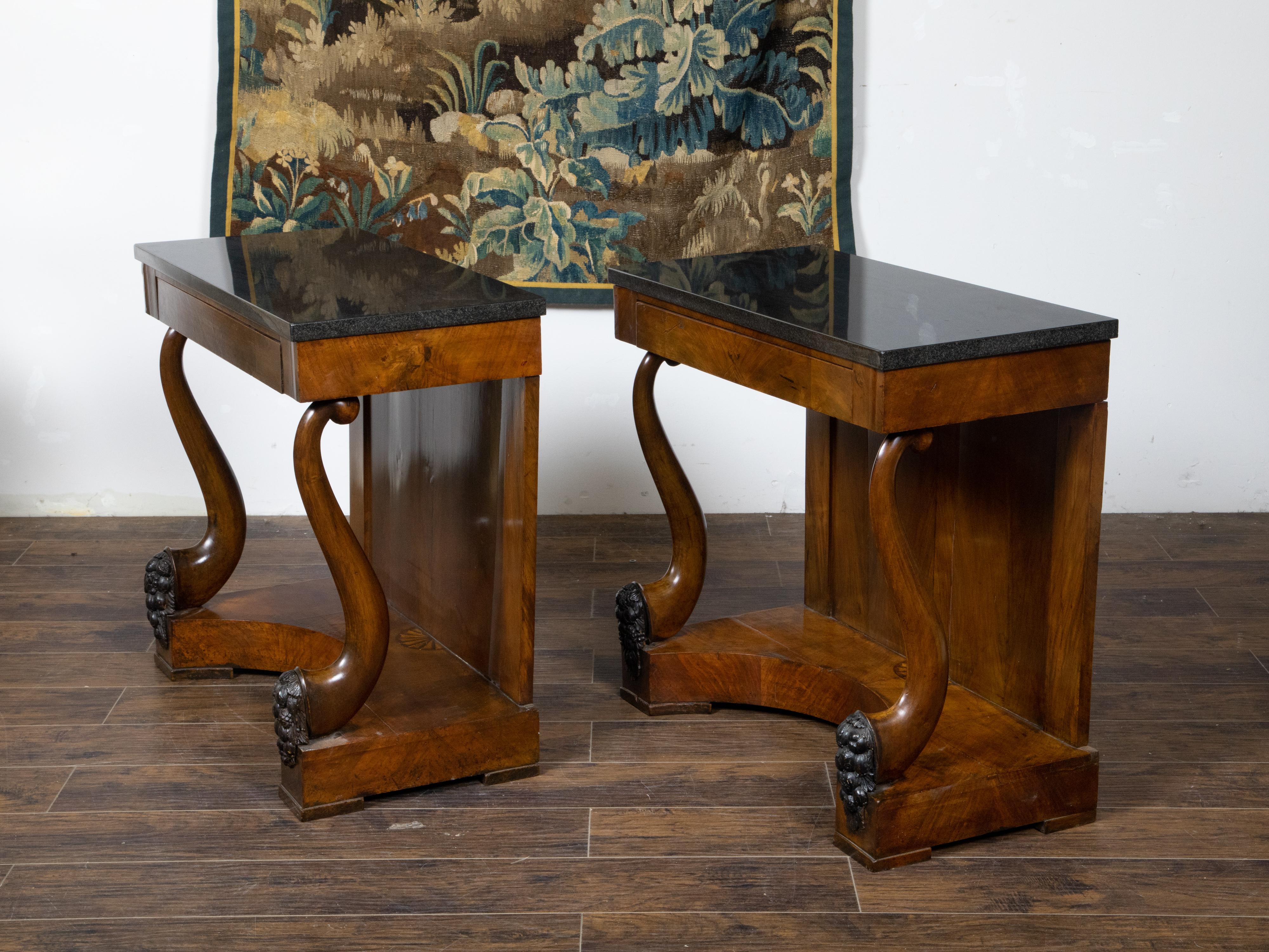 A pair of Austrian Biedermeier period walnut console tables from the 19th century, with black marble tops, scrolling voluted leg supports, ebonized carved accents with grapes and inlaid fan motif. Created in Austria during the Biedermeier period,