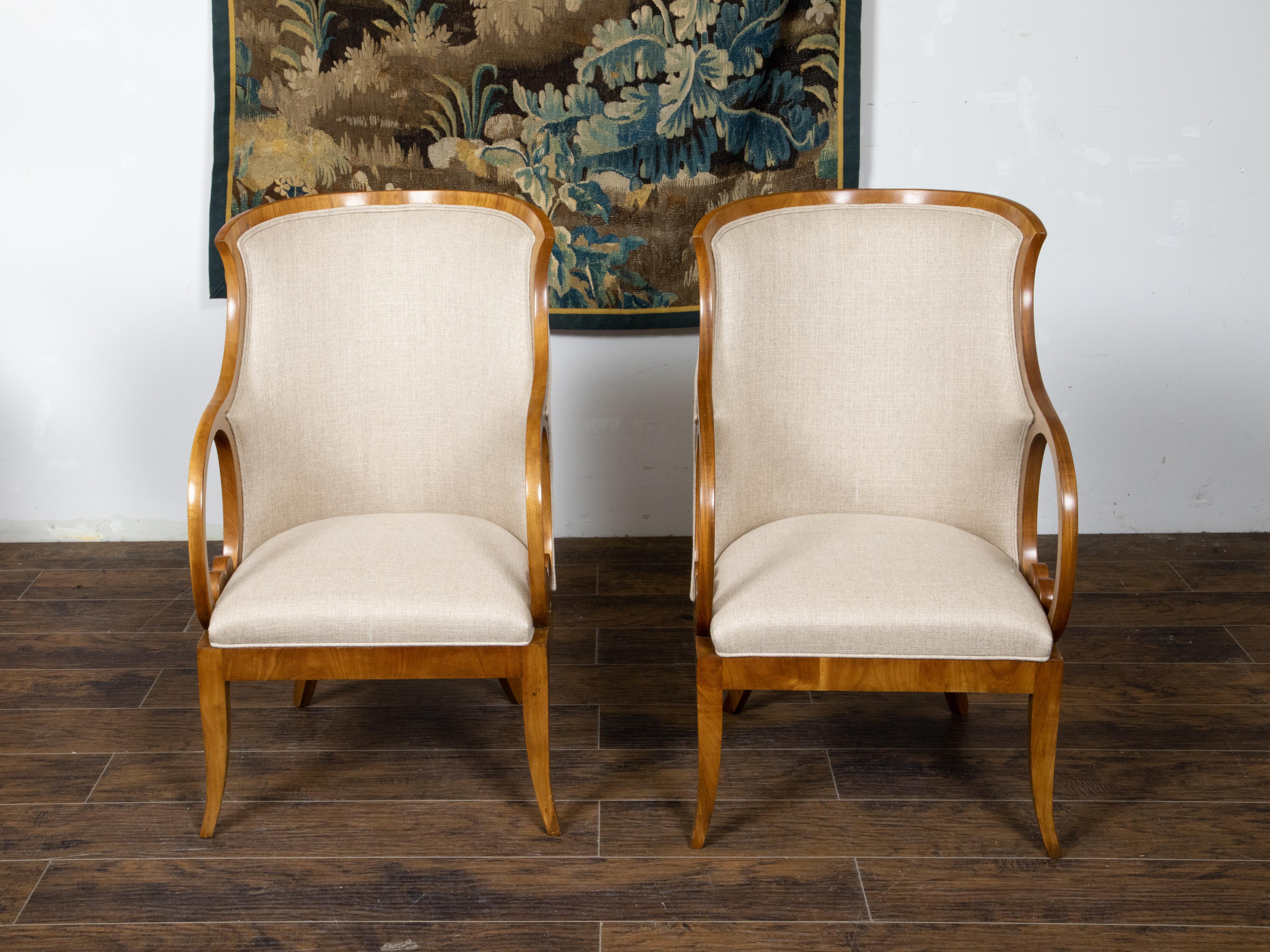 A pair of Austrian Biedermeier period bergère armchairs from the 19th century, with carved looping arms, saber legs and new upholstery. Created in Austria during the Biedermeier period in the 19th century, each of this pair of armchairs features a