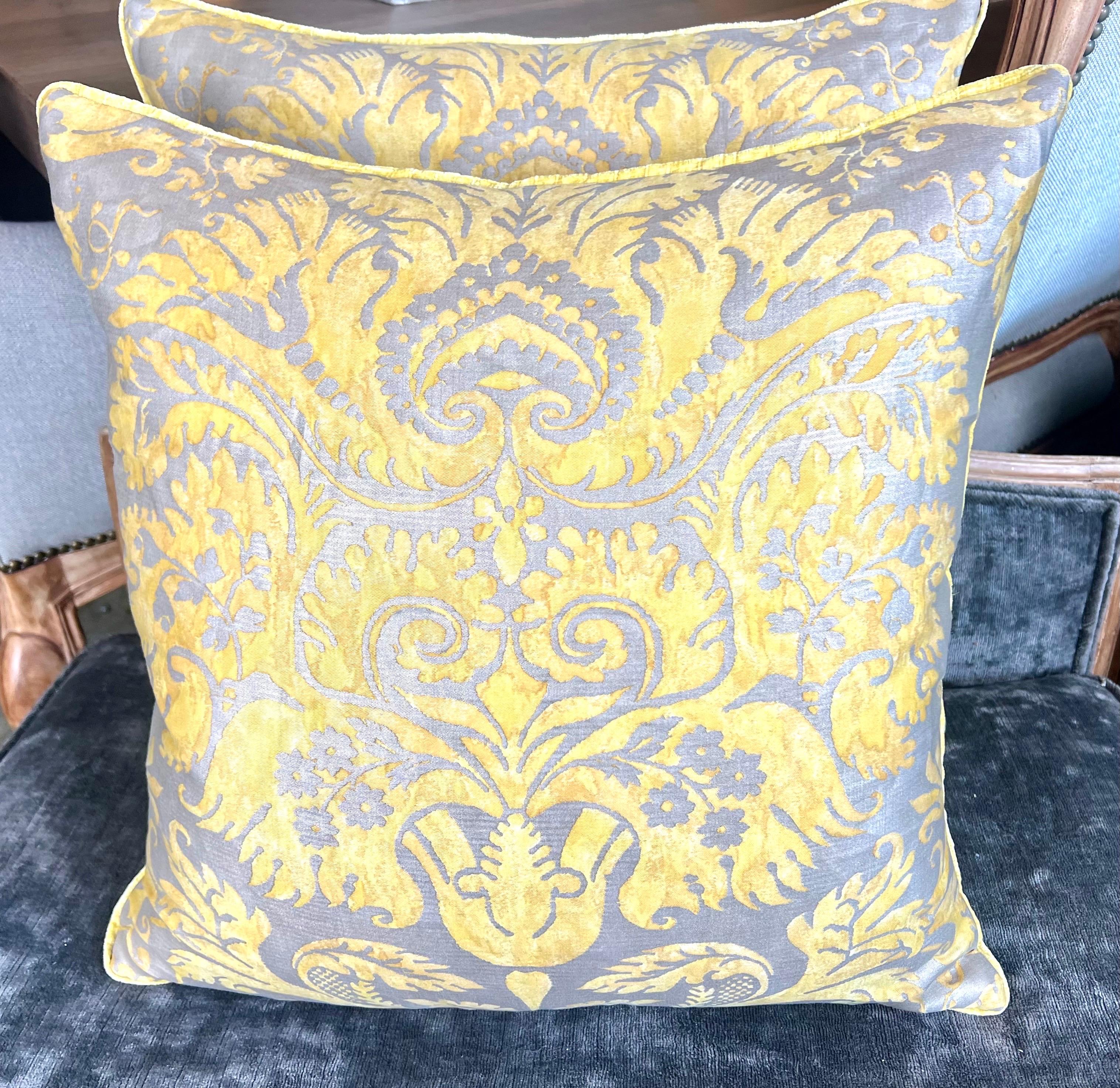 Une paire de coussins floraux exquis de Fortuny, où chacun témoigne du luxueux jeu de couleurs et de motifs, sur un fond argenté envoûtant.  Ces coussins brillent avec une palette jaune safran, créant un design floral vibrant et invitant qui capture