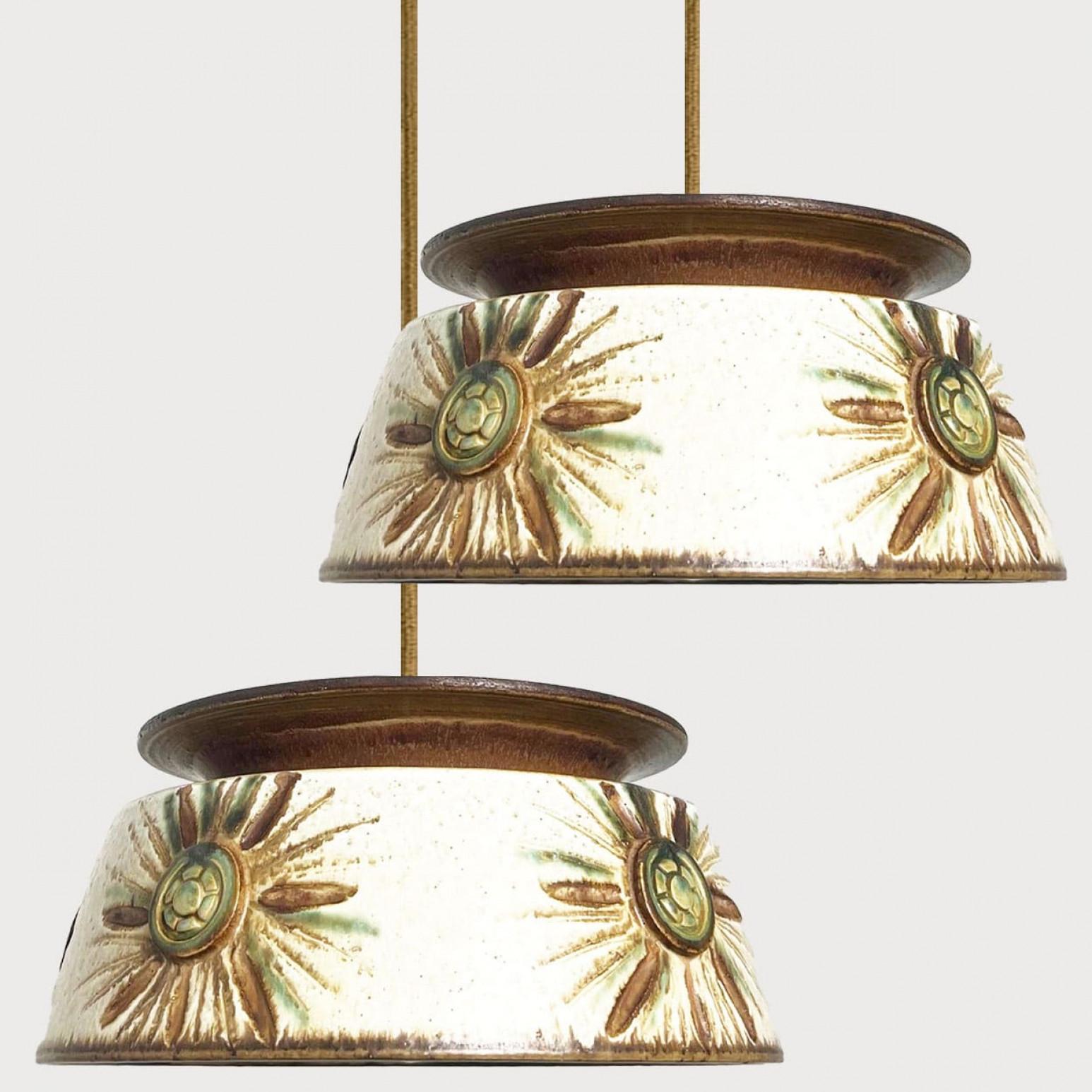 L'une des deux superbes lampes suspendues rondes de forme inhabituelle, fabriquées dans les années 1970 au Danemark avec des céramiques aux riches couleurs bleu, vert, beige et marron.

Avec de beaux câbles d'acier fragiles et des détails en bois.