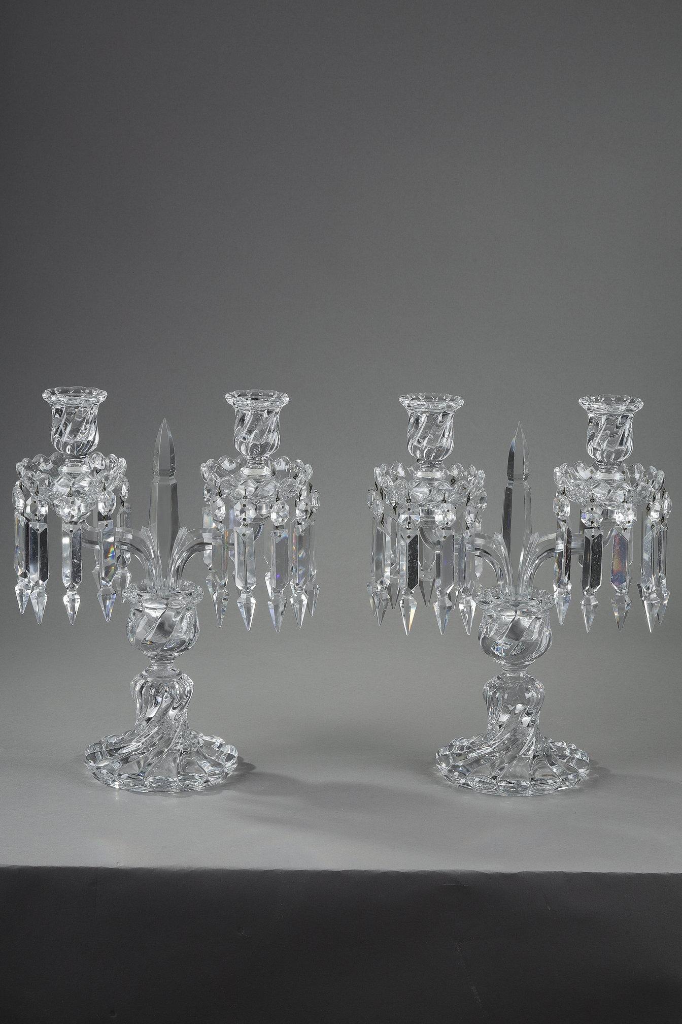 A pair of Baccarat crystal girandoles with two light arms adorned with triangular prism-shaped pendants ending in a point. The base and bobèches are twisted. The upper part of the shaft ends in a point. The pair is engraved with Baccarat pastilles