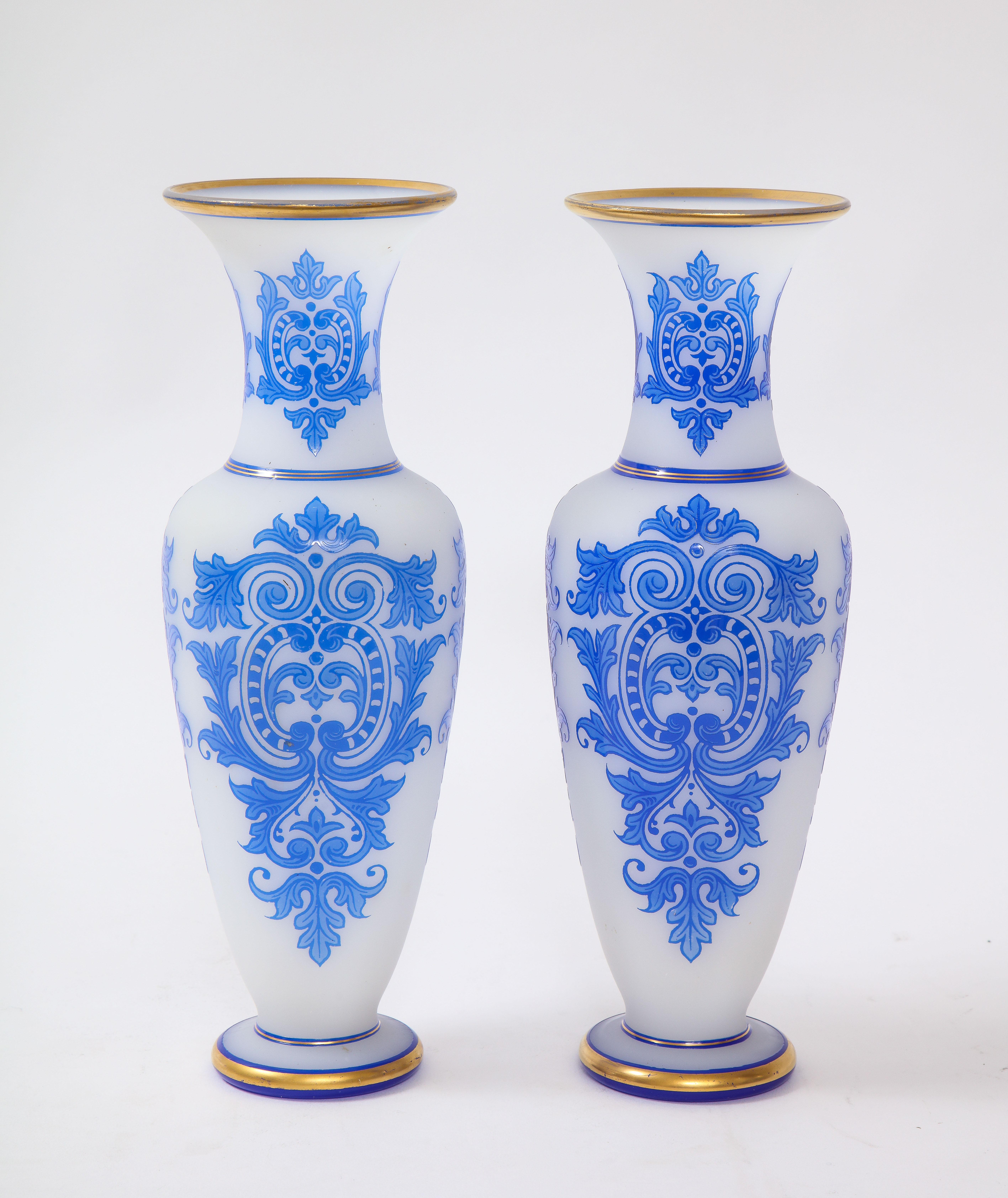 Une fabuleuse paire de vases Baccarat de style Louis XVI du 19ème siècle, à double recouvrement de bleu sur blanc opalin clair avec une décoration en or peint à la main 24k. Chaque vase est de forme élancée avec un fond blanc opalescent et un