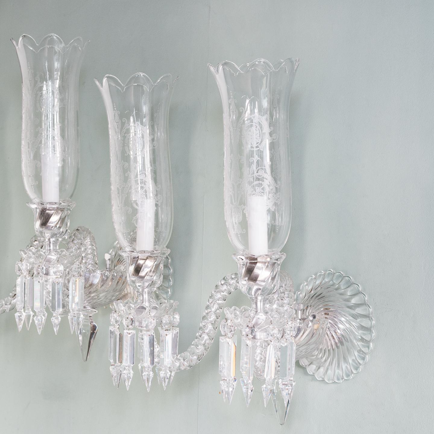 A pair of Baccarat glass wall appliques, each with gadrooned backplate and scallop-edged gadrooned bowl issuing two wrythen arms, the drip-pans hung with pendant droplets, each with etched glass storm shade.