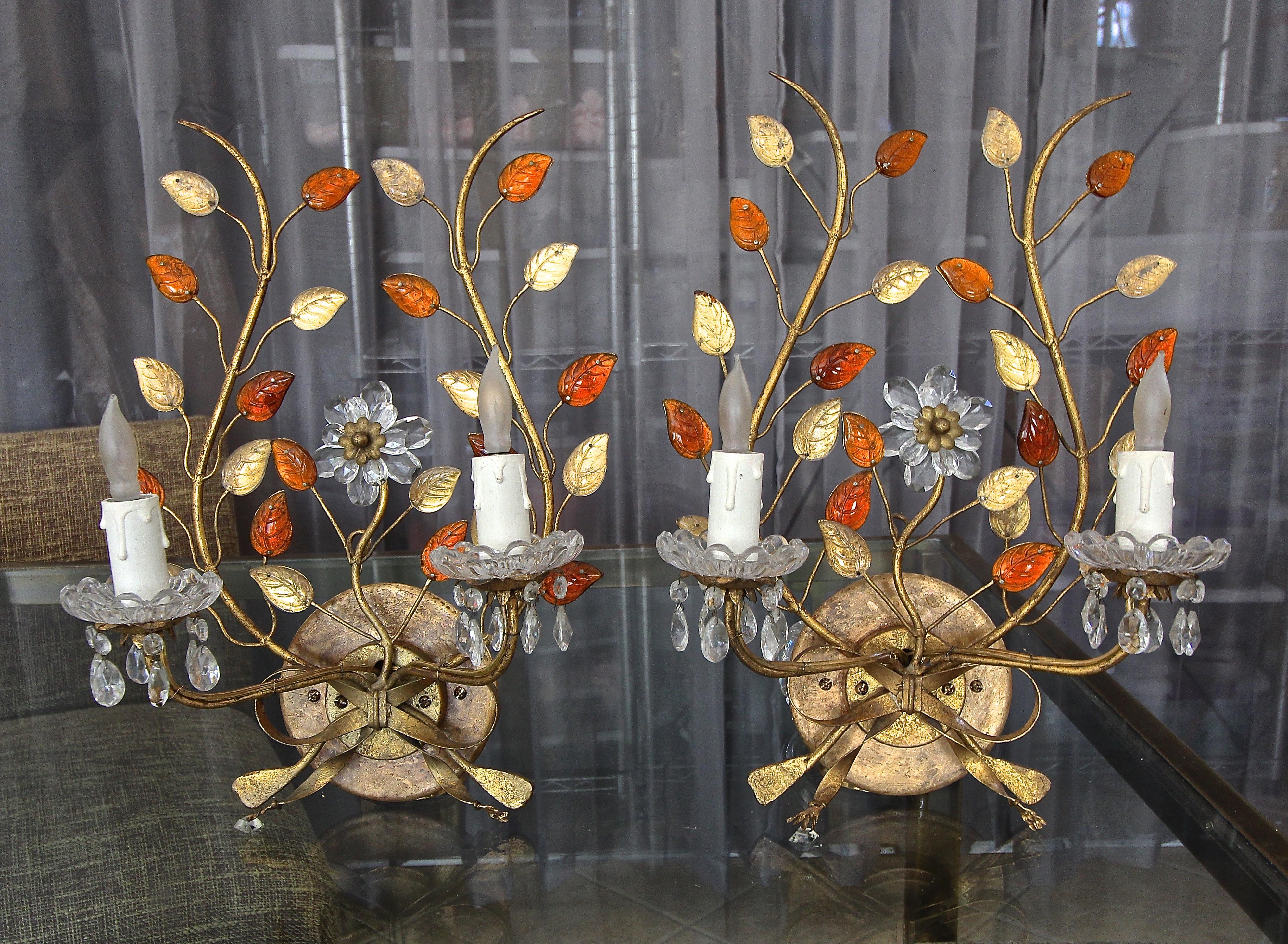 Pair of elegant 1940s gilt metal two-light wall sconces with a floral and leaf bouquet design. Detailing of the sconces includes clear and amber/ deep orange glass leaves, and crystal cup bobeches surrounded by dangling cut crystals prisms. Each