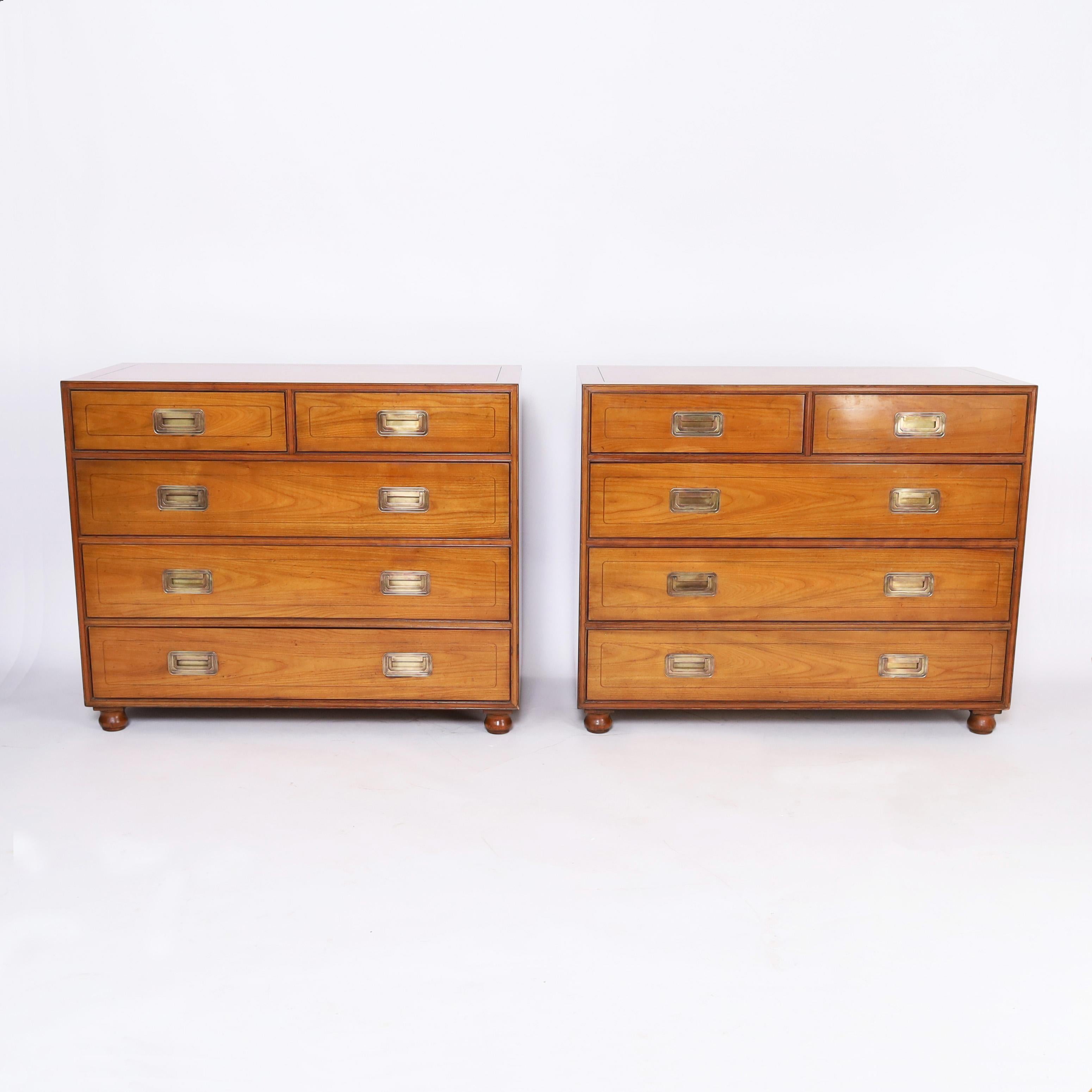 Impressive pair of chests or commodes crafted in fruitwood in a sleek modern form with hints of tradition having brass campaign style hardware and classic turned feet. Signed Baker in a drawer.