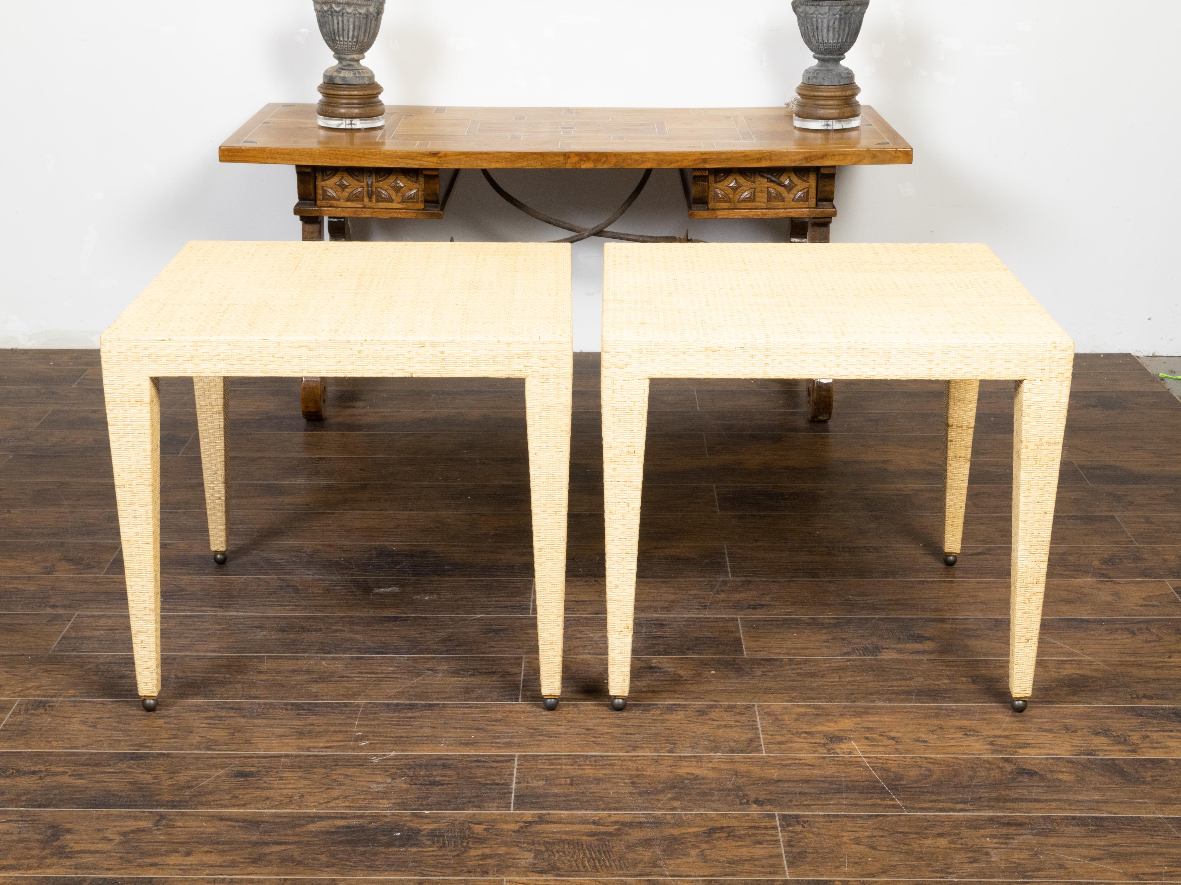 A pair of vintage Baker Furniture Company wicker side tables from the mid 20th century, with tapered legs and petite ball feet. Made in the USA by the Baker Furniture Company during the Midcentury period, this pair of side table charms us with its