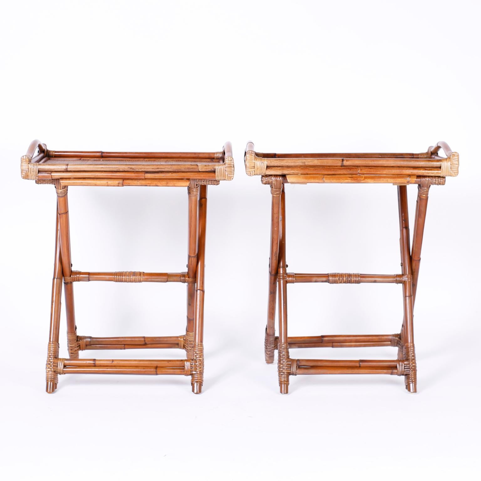 British colonial serving stands with removable trays having handles, grasscloth surfaces, and reed wrapped corners sitting on bamboo folding X-form bases with reed wrapped joints.