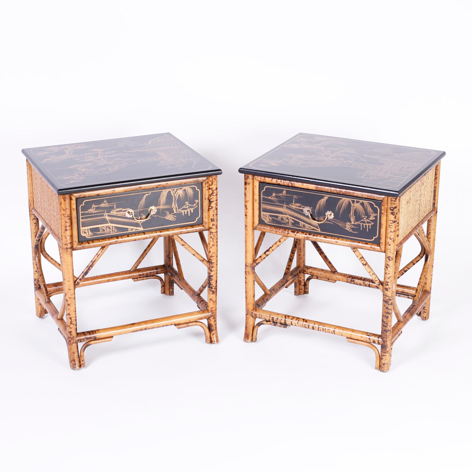 Pair of midcentury one drawer nightstands or end tables with burnt bamboo frames, grass cloth panels, black lacquer tops, and drawer fronts hand painted with scenes of architecture and trees.